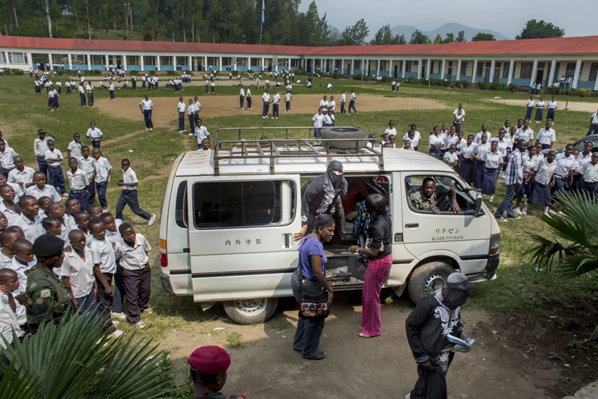 Students flock around a van delivering women to testify in a makeshift courtroom set up in the auditorium of a Catholic school in Minova. Victims could not afford a trip to Goma, more than 30 miles away, so the court went to them in Minova. © Diana Zeyneb Alhindawi