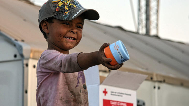 A boy hands face cream, distributed by the Red Cross, to his mother in Macedonia. © IFRC / John Engedal Nissen