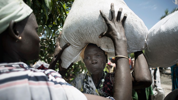 Unity State, Leer, South Sudan. A man helps a woman to heave a bag of sorghum on her head at an ICRC food distribution. ©Jacob Zocherman/ICRC