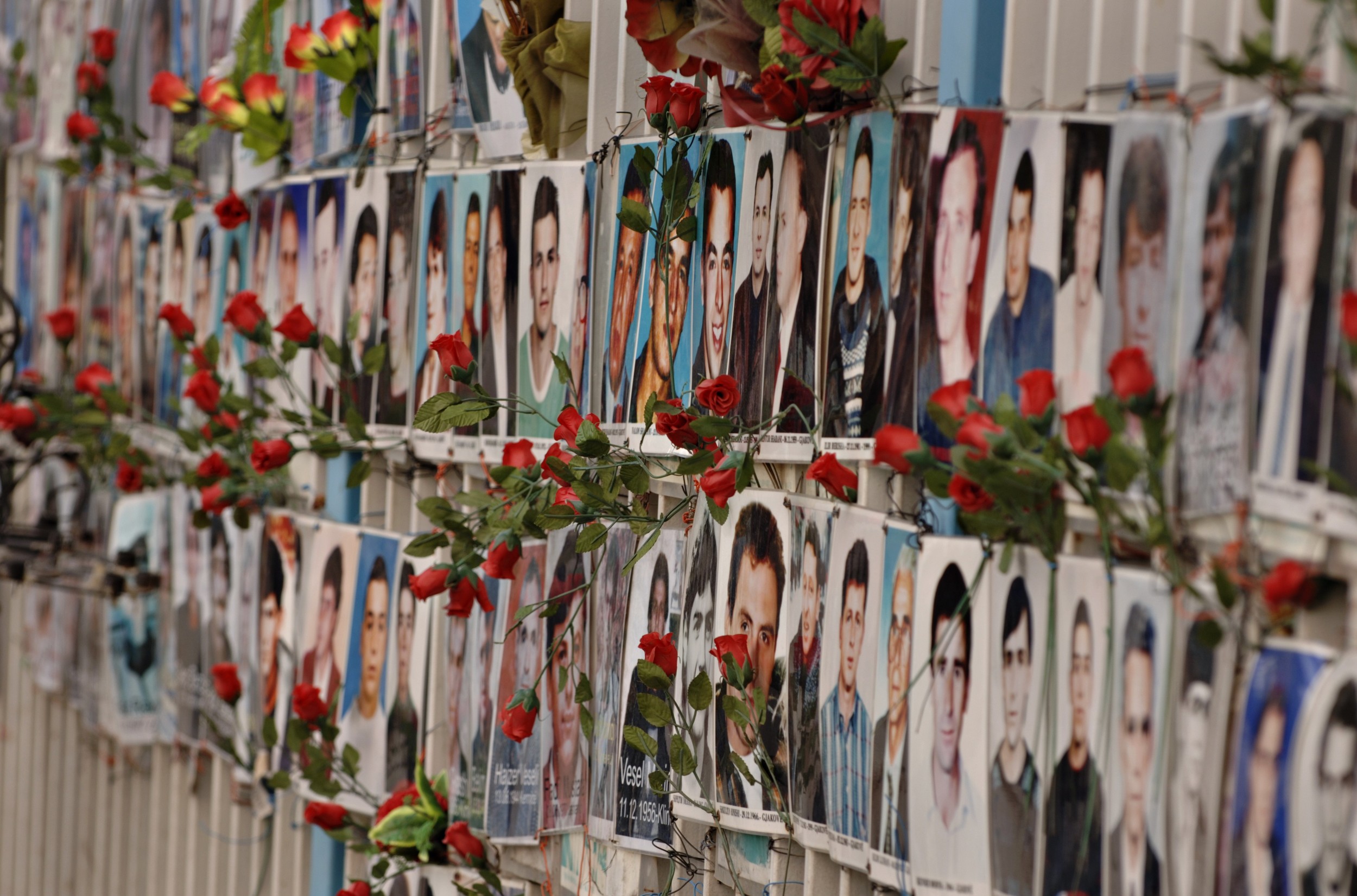 Pristina. Pictures of missing persons hanging on a fence outside a public building. Fresh flowers are attached to many of the portraits of people that have been missing since the war that ended in 1999. ©SALTBONES, OLAV/ICRC