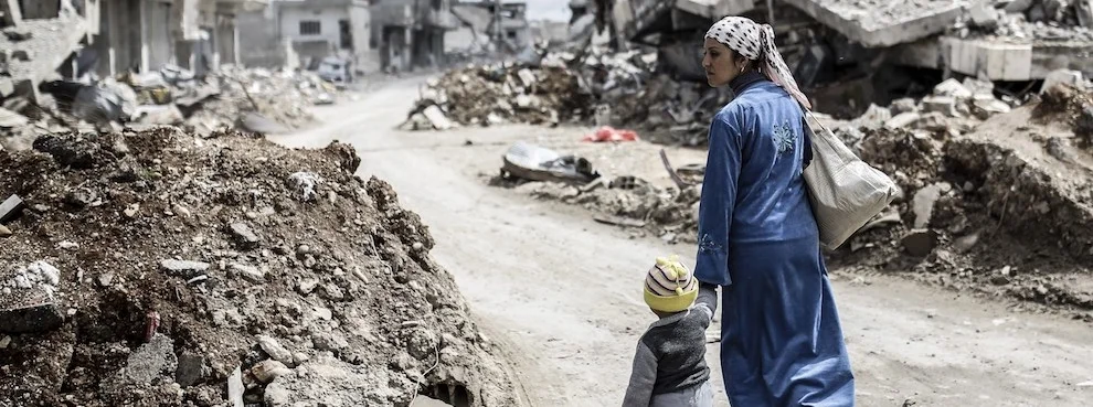 A Kurdish Syrian woman walks with her child past the ruins of the town of Kobane, also known as Ain al-Arab, on March 25, 2015. (YASIN AKGUL/AFP/Getty Images)