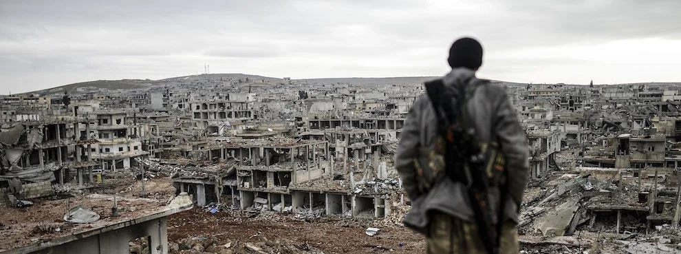 A Kurdish marksman stands atop a building looking at the destroyed Syrian town of Kobane, also known as Ain al-Arab, on January 30, 2015. (BULENT KILIC/AFP/Getty Images)