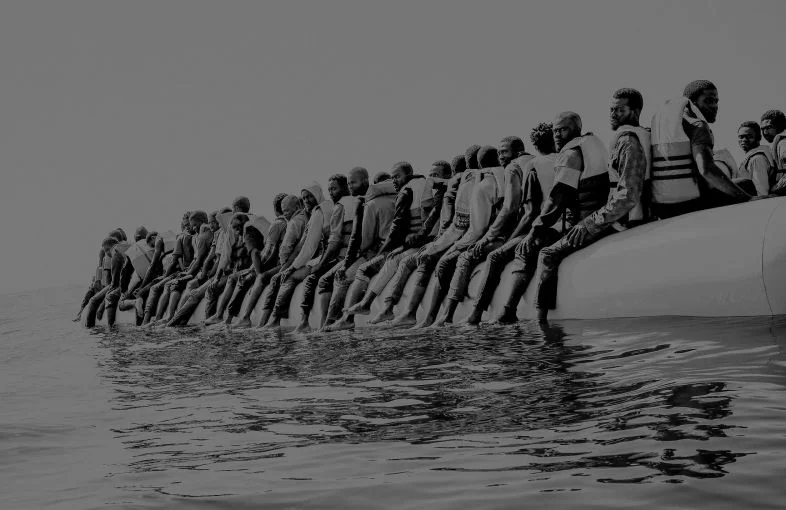 Roughly a hundred and fifty people wait to be rescued from an inflatable dinghy in the Mediterranean Sea, twenty miles north of Libya. The boat left with only enough fuel to reach international waters. Image by Ben Taub. Libya, 2016.