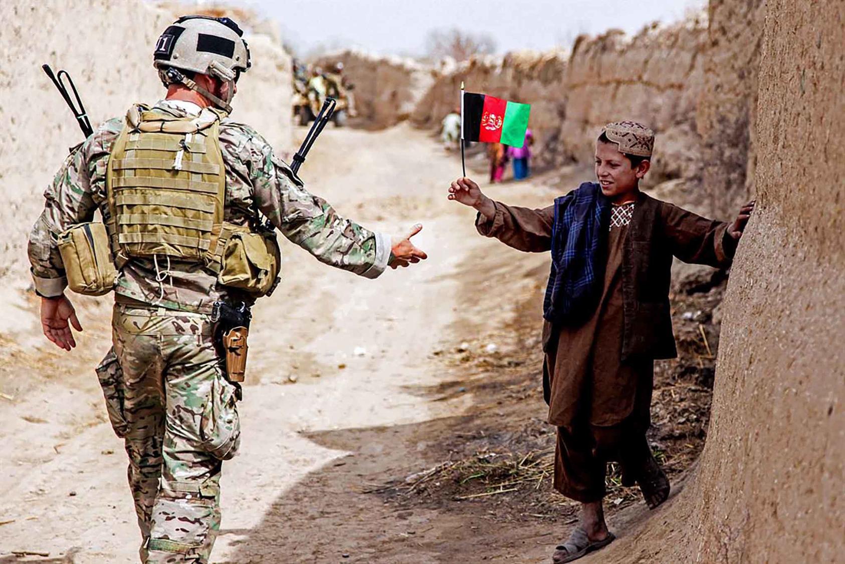 An Afghan child waves a flag at a member of coalition forces as he patrols to a medical clinic led by Afghan national security forces in the Panjwai district of Afghanistan’s Kandahar province. (Photo Courtesy: Department of Defense)