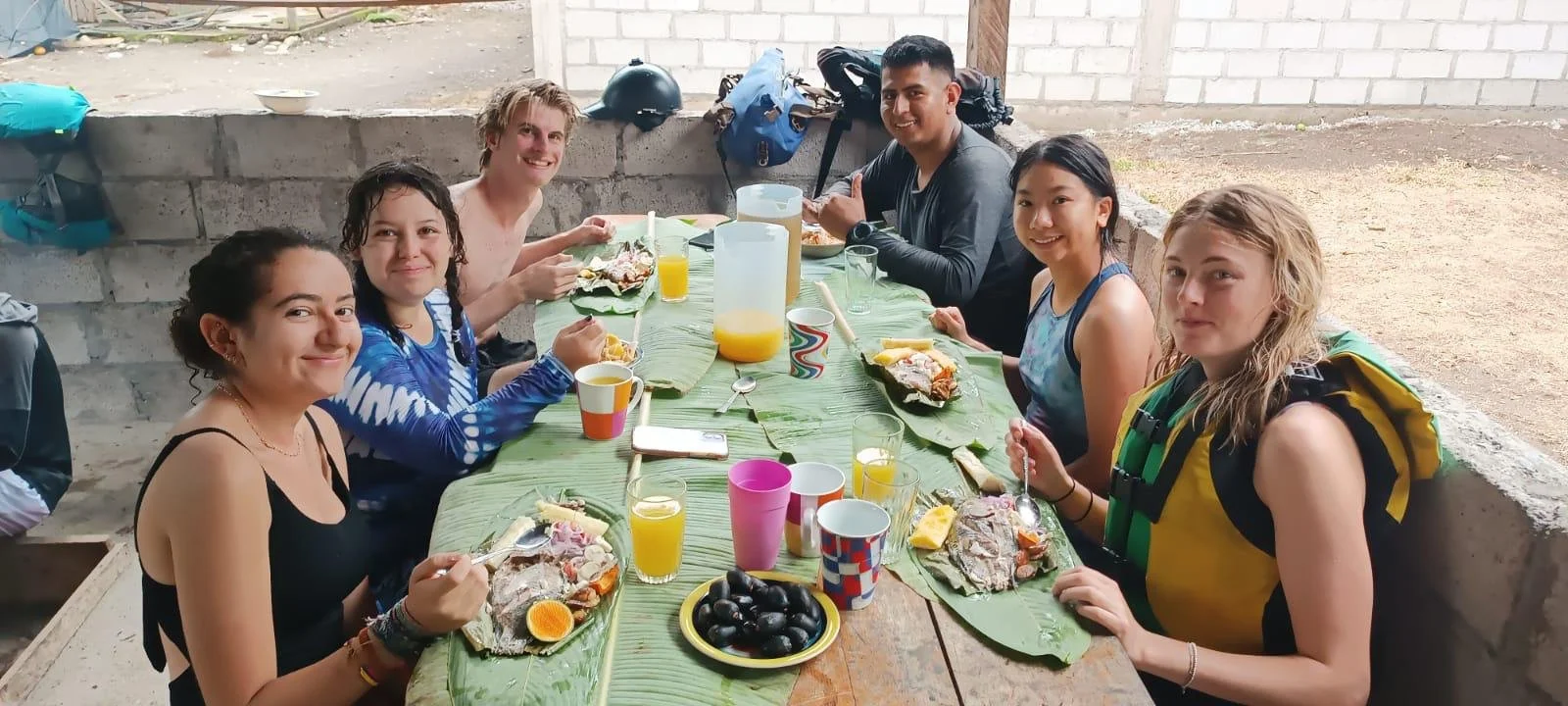 group of volunteers eating a traditional meal outside on banana leaves.