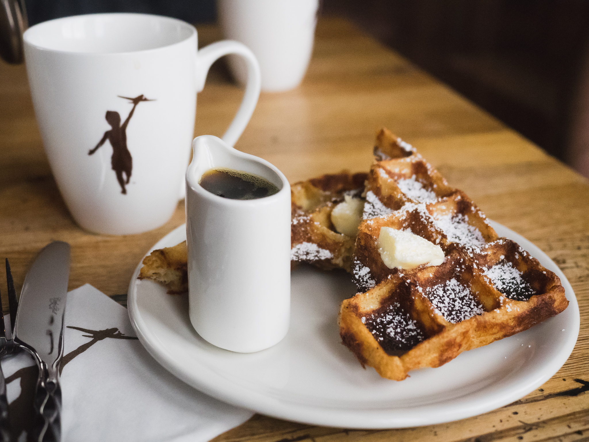 french press coffee and a waffle with butter, powdered sugar and maple syrup.