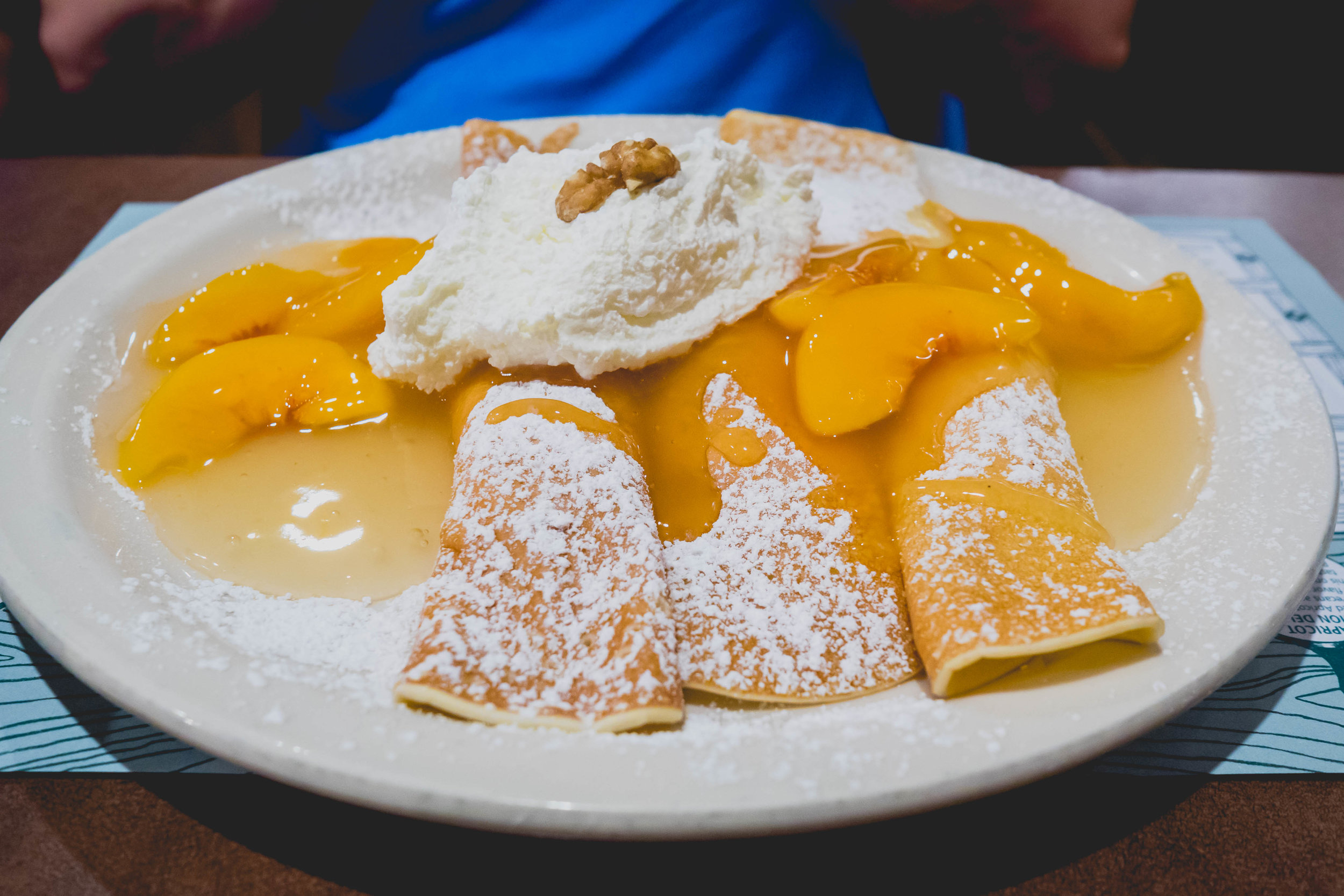 peach delight : thin rolled crepes filled with ricotta, cream cheese, peaches, topped with peach compote, powdered sugar, whipped cream.