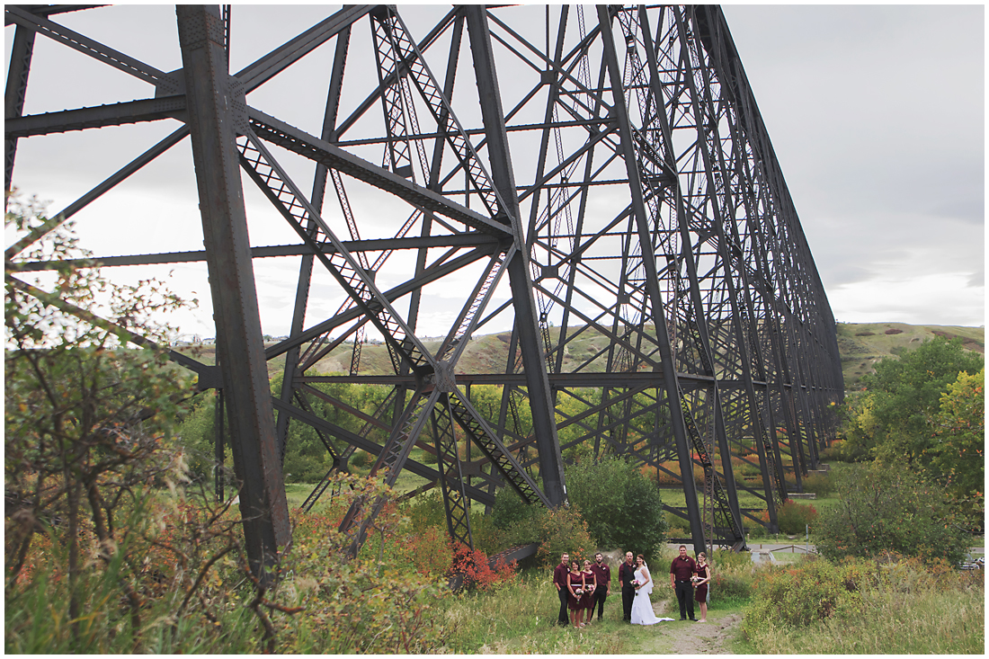Lethbridge High Level Bridge wedding party A stunning Fall wedding in Lethbridge Alberta - a religious church ceremony at the URC Church with stained glass windows, a quick stop at the Wooden Shoe for lunch and bridal party pictures at Indian battle park. #albertawedding #lethbridge #redwinewedding #redcolourscheme #babiesbreathboquet #indianbattlepark #woodshoe #overcastwedding #fallwedding #kissingcouple #brideandgroom #emotionalwedding #church #churchceremony