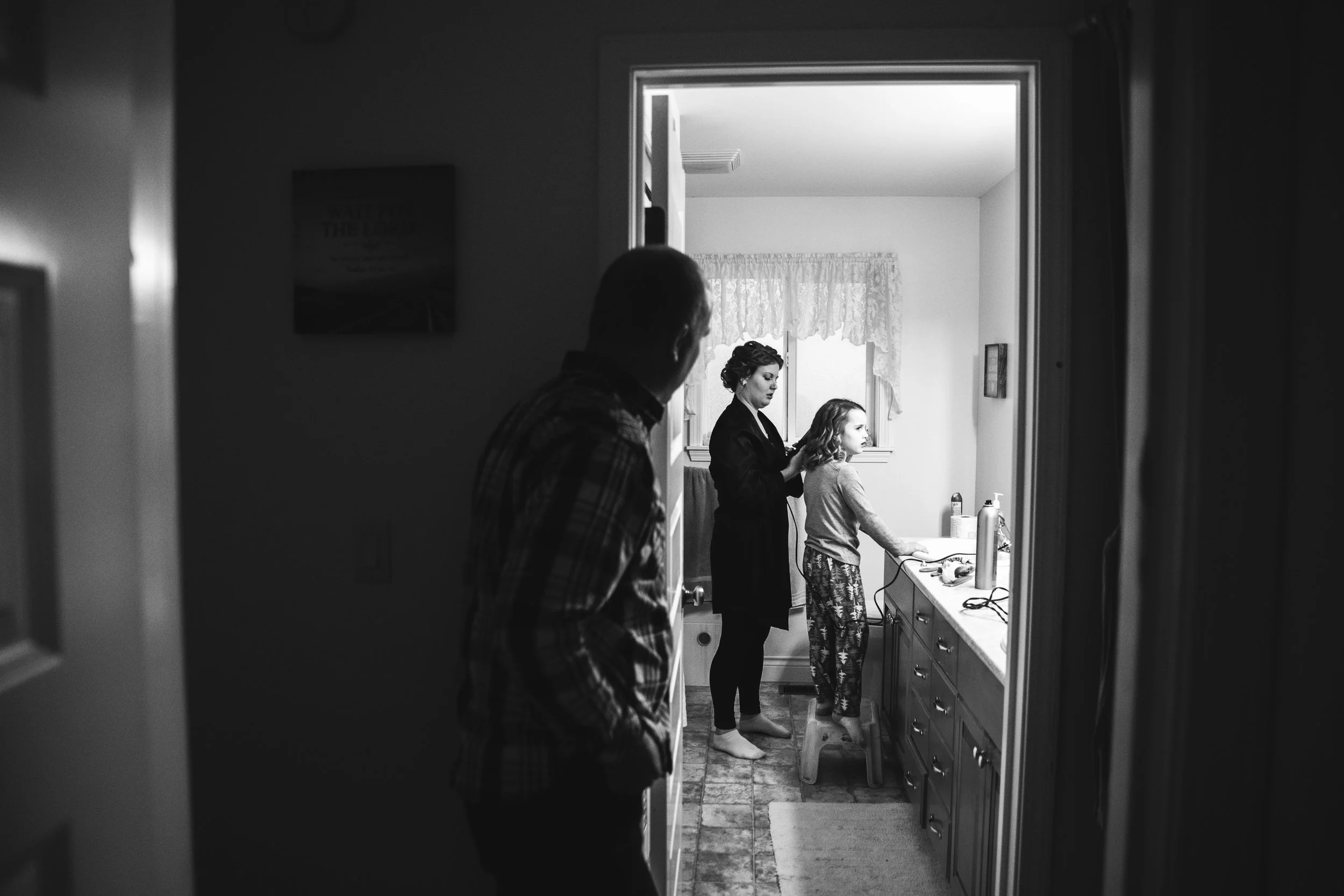Bride doing her flower girls hair in the bathroom the morning of the wedding> A rainy forest wedding in Lynden Washington, featuring teal blue accents, rustic details, umbrellas and a large bridal party. #rain #wedding #lynden #washington #umbrella #spring #teal #grey #brown #trees #romantic #documentarywedding #unposed #romanticposes #couple #largebridalparty Photography by Christina Voorhorst of Mimsical Photography. Do not alter, crop, edit or share these images without proper credit or permission. www.mimsicalphotography.com 