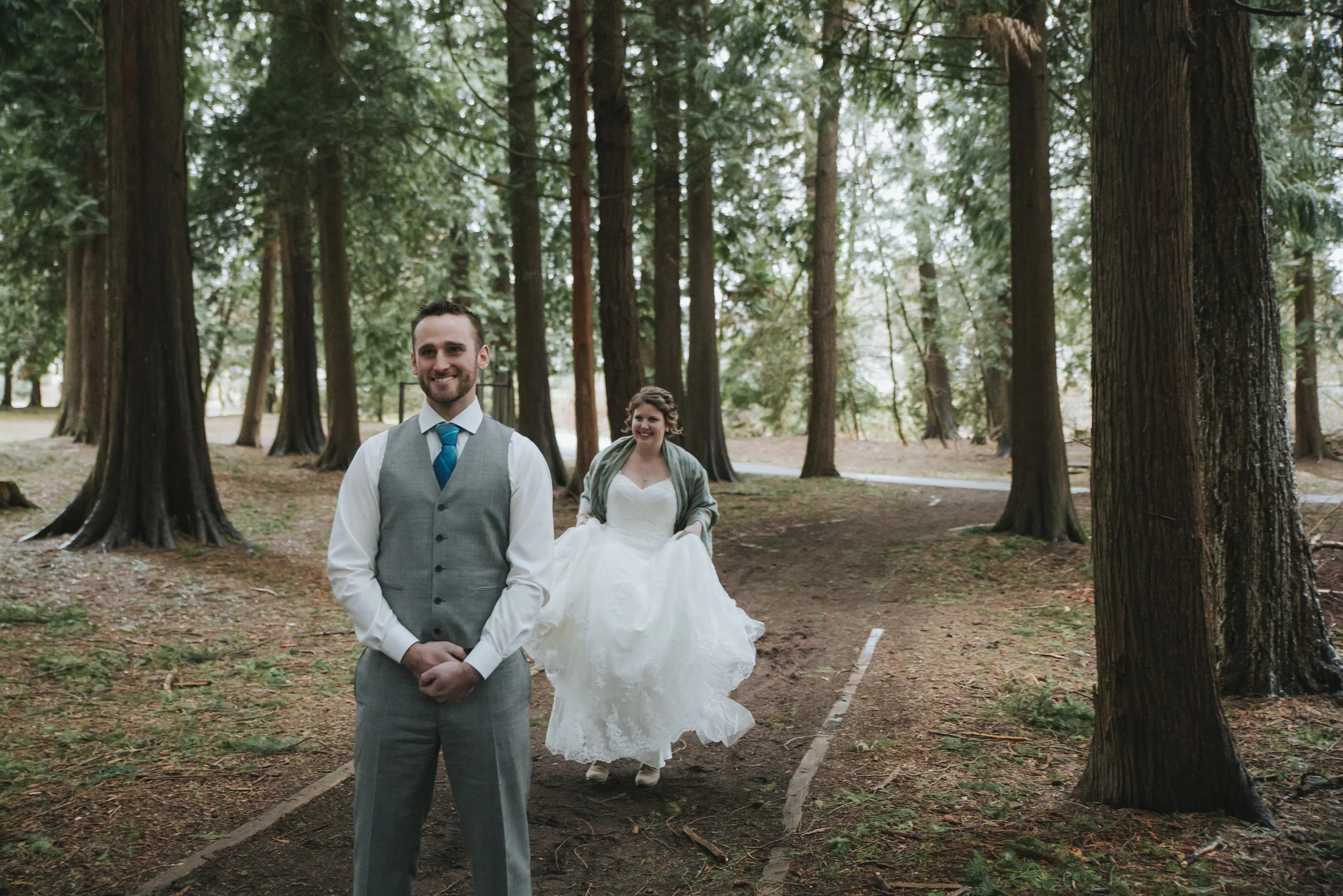 First look bride approaches from behind. A rainy forest wedding in Lynden Washington, featuring teal blue accents, rustic details, umbrellas and a large bridal party.#rain #wedding #lynden #washington #umbrella #spring #teal #grey #brown #trees #romantic #documentarywedding #unposed #romanticposes #couple #largebridalparty Photography by Christina Voorhorst of Mimsical Photography. Do not alter, crop, edit or share these images without proper credit or permission. www.mimsicalphotography.com 