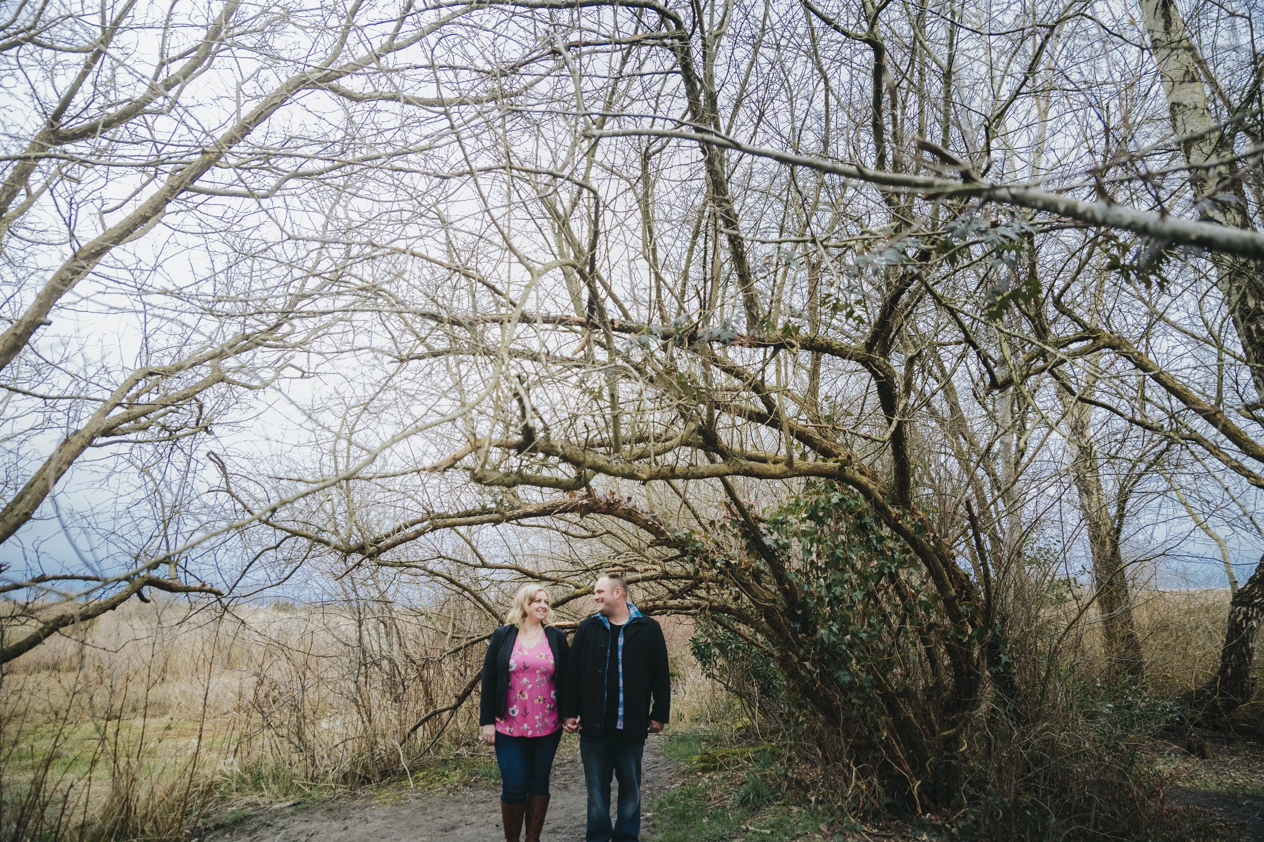 Cloudy engagement session at Garry Point Park in Richmond, BC. Couple under a natural tree arch in early spring Photography by Christina Voorhorst of Mimsical Photography #westcoastphotographer #engagement #ring #couple #ocean #cloud #overcast #romantic #poses