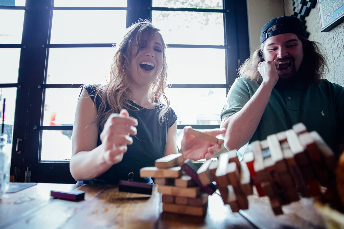 Jenga tower falling down during couple's date at Storm Crow Tavern Storm Crow Tavern Documentary Engagement Photography, Nerd Bar, Board Games by Mimsical Photography. Real stories about Real Couples that are just as unique as they are. #unique #vibrant #personality #nerd #princess #ecclectic #gamer #couple #tavern #vancouver #candid #storytelling