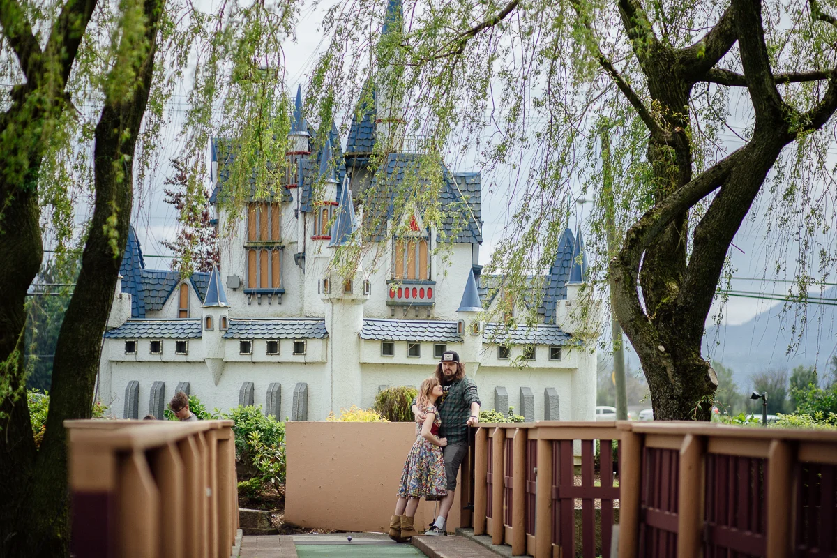 Standing by the Iconic Castle from Castle Fun Park Castle Fun Park Documentary Engagement Photography, minigolf date by Mimsical Photography. Real stories about Real Couples that are just as unique as they are. #unique #vibrant #personality #nerd #princess #ecclectic #gamer #couple #minigolf #vancouver #candid #storytelling #connect #datesforcouples #arcade #arcadedate