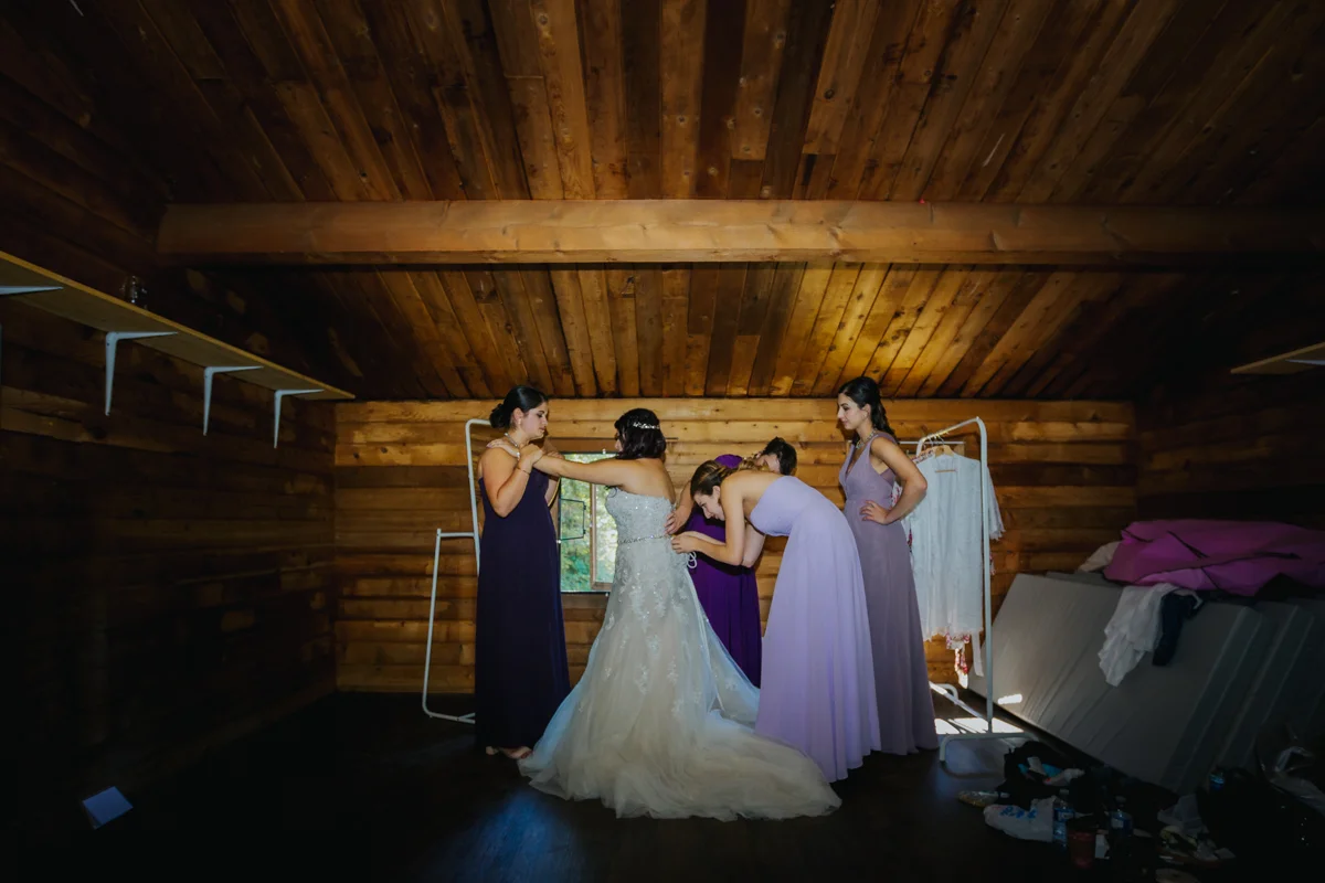 bridesmaids helping bride get dressed Mimsical Photography Documentary Wedding Photography, Camp Howdy, Belcarra Provincial Park, North Vancouver. Purple and Grey Wedding Colours, Natural Greenery, Rustic Details, Summer, Lace and chiffon, big wedding, greek, lower mainland, british columbia, real, genuine, candid