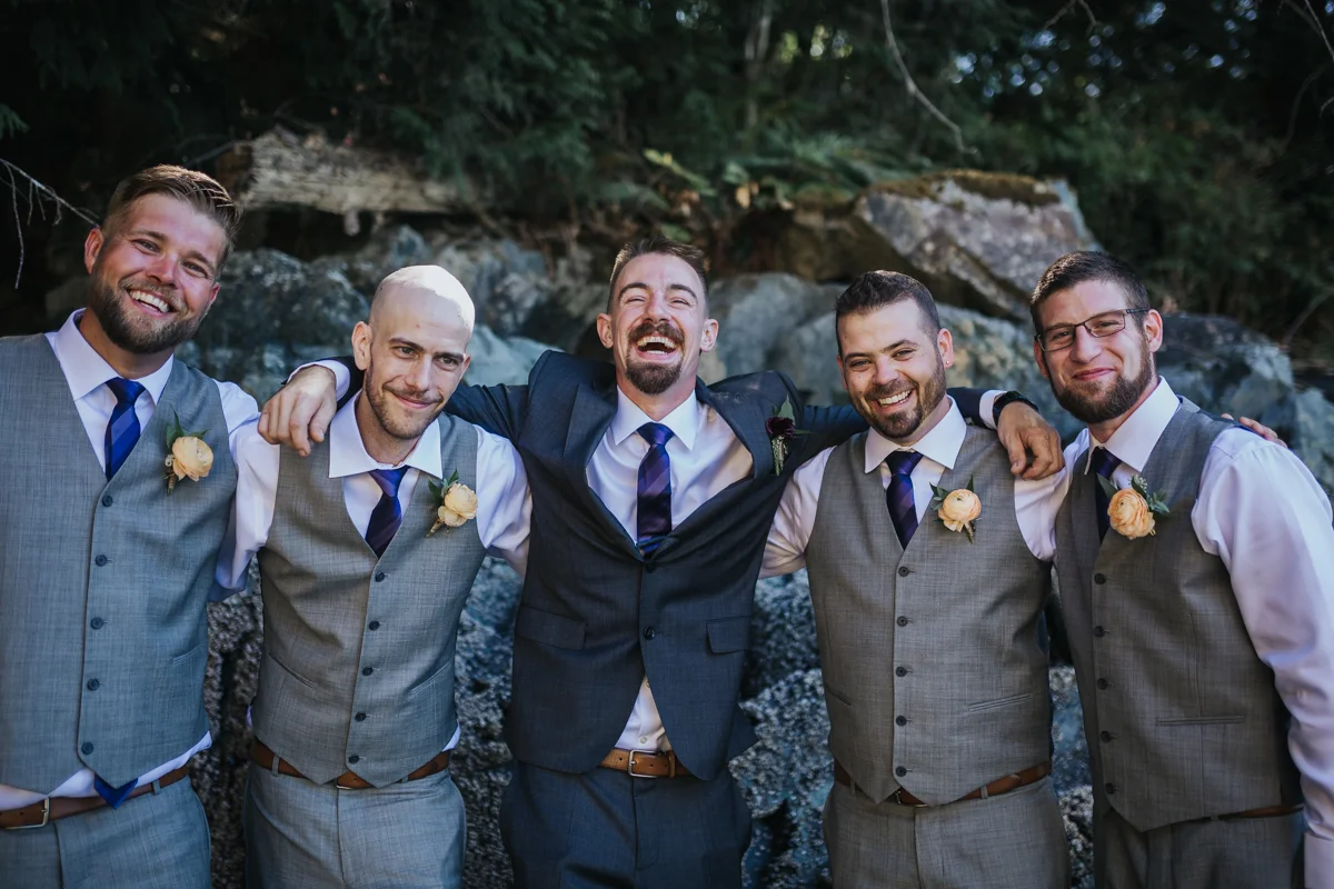 groomsmen laughing with groom in group hug - light grey vest and purple ties. orange rose boutinere Mimsical Photography Documentary Wedding Photography, Camp Howdy, Belcarra Provincial Park, North Vancouver. Purple and Grey Wedding Colours, Natural Greenery, Rustic Details, Summer, Lace and chiffon, big wedding, greek, lower mainland, british columbia, real, genuine, candid
