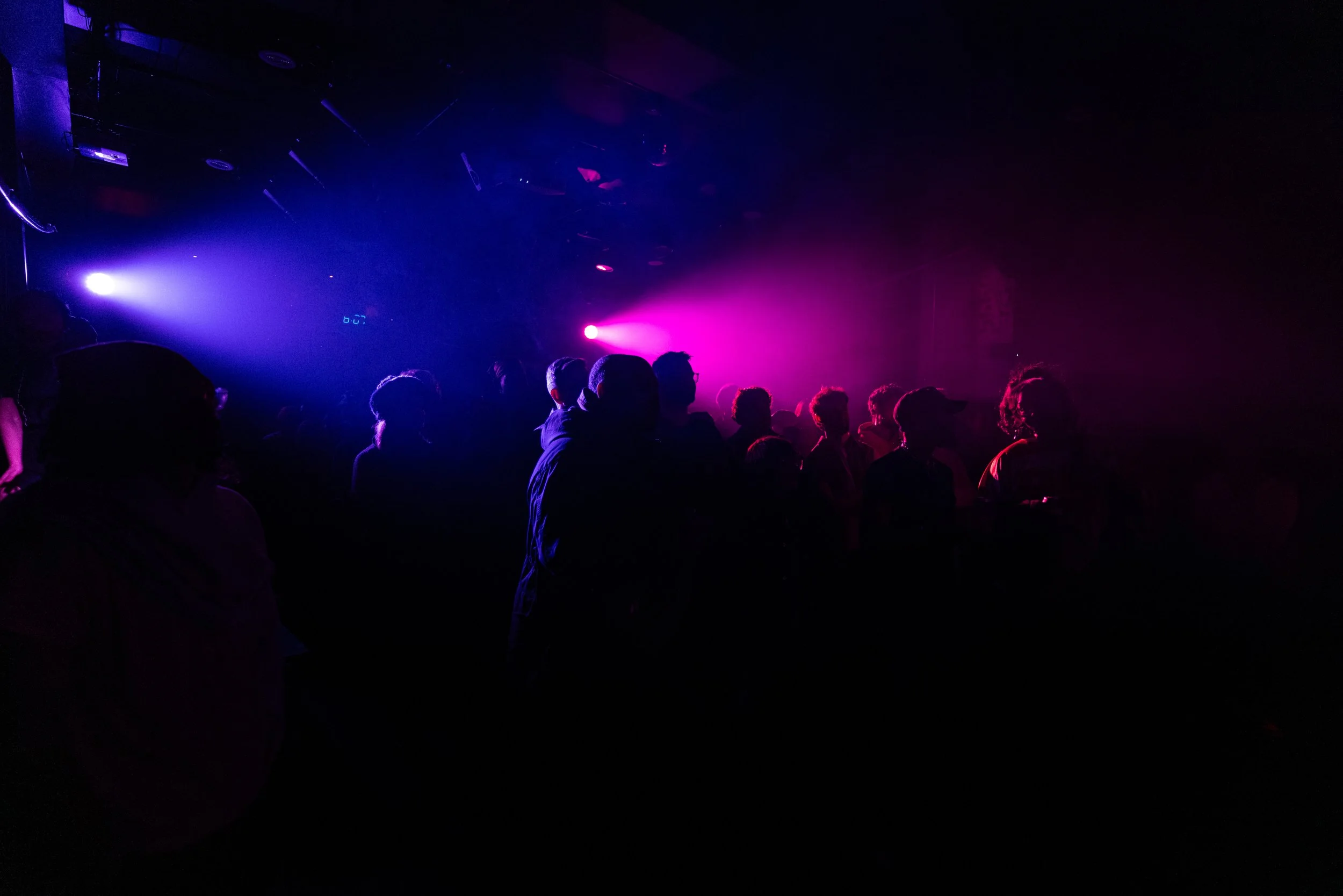 Silhouettes of people in a dark nightclub with colorful purple, blue, and pink lights.