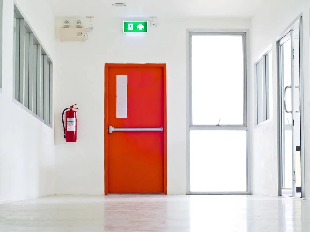 Red passive fire protection door with white walls and big windows. There is a red fire exntinguisher beside the door.