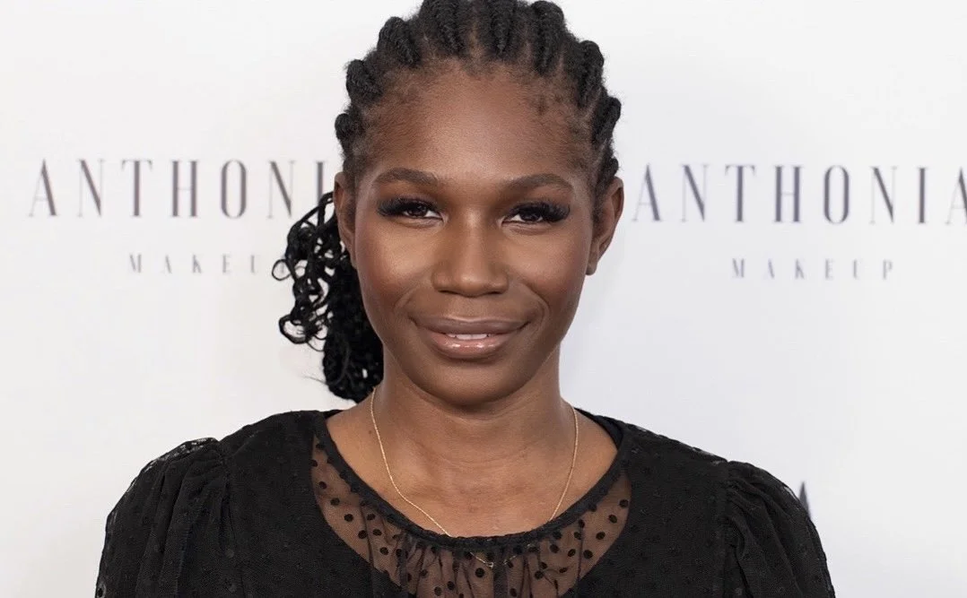 A woman with dark skin, styled in braided hair, wearing a black dress with polka dot sheer details, standing in front of a white background with text.