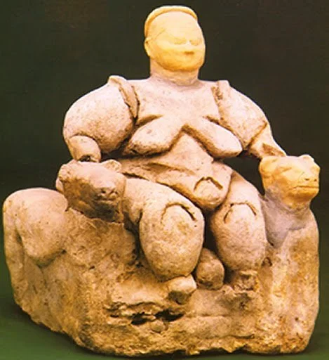 A stone sculpture of a seated figure with no facial features, holding objects in each hand, against a dark background.