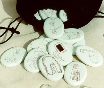 Collection of small white stones with engraved religious symbols and figures, arranged near a black cord or string.