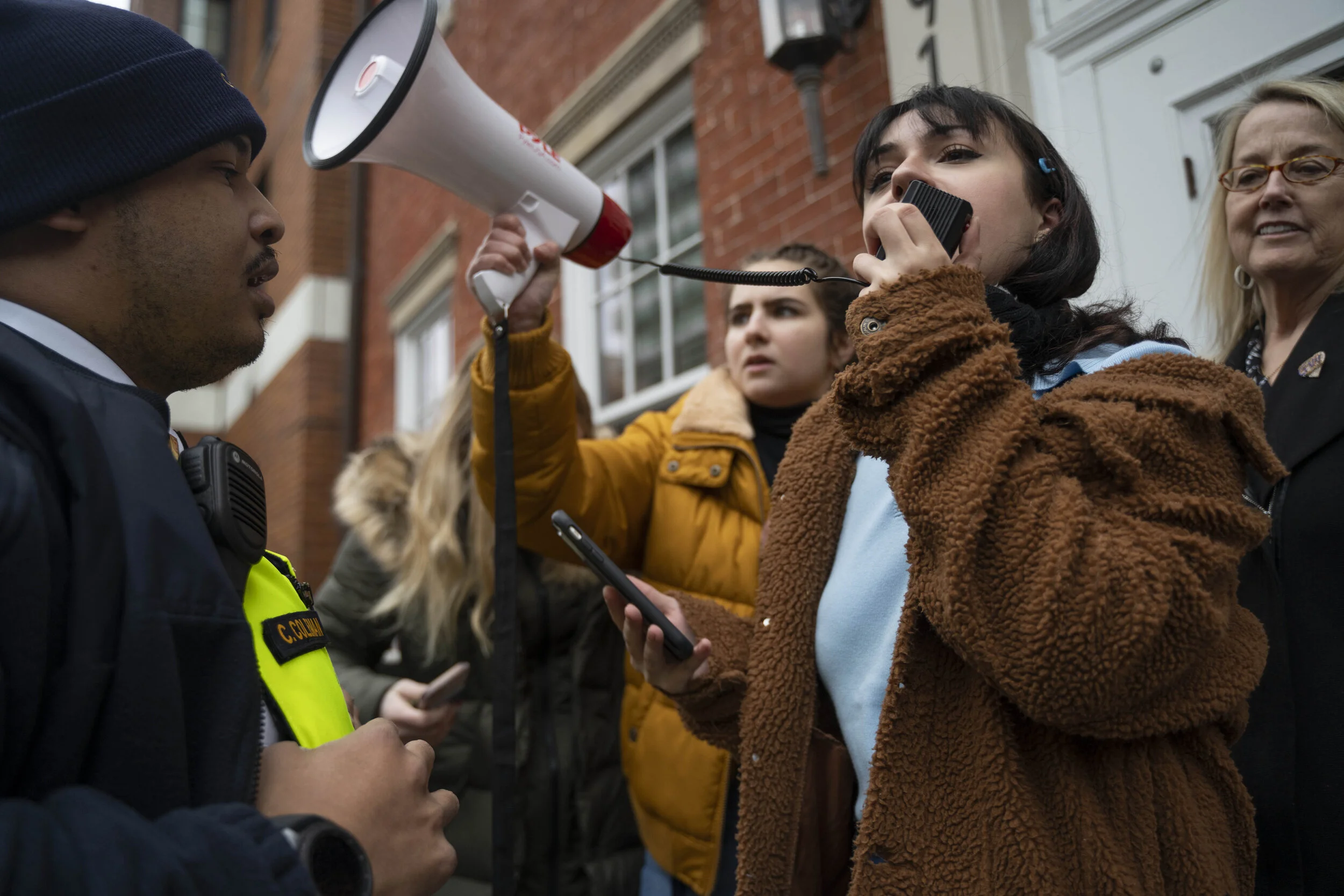 Sunrise GW protesters stand at the door of 1918 F Street with a megaphone as a GWPD officer confronts them on February 5, 2020.