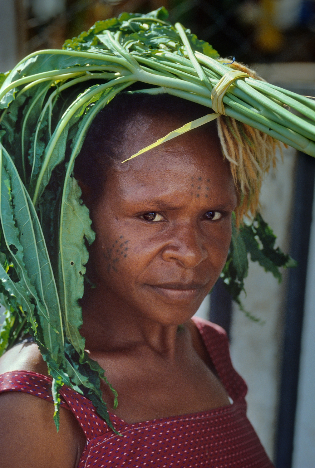 Her arms full of other groceries, an unidentified woman carries food on her head in Port Moresby, Papua New Guinea.
