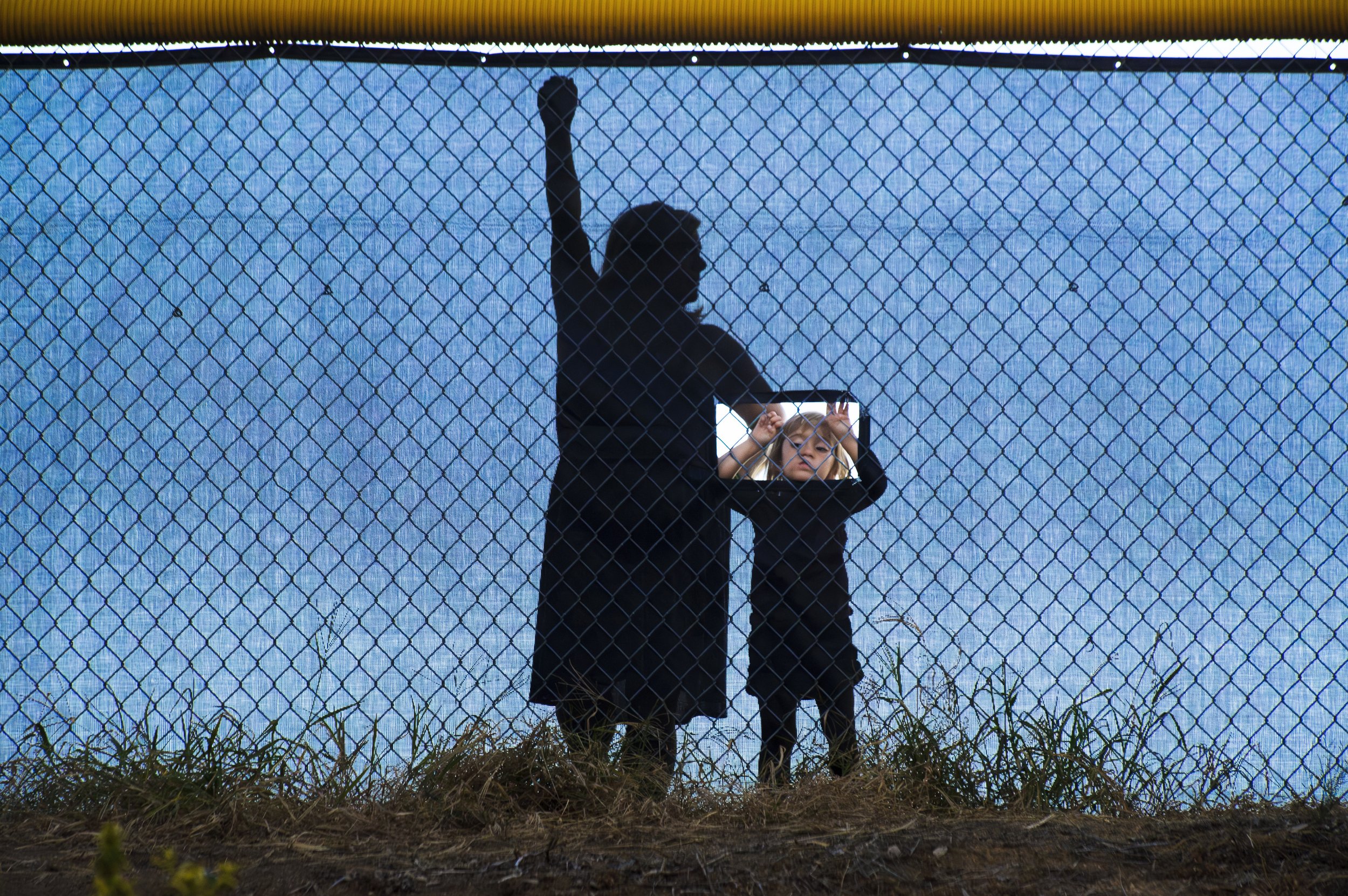  Mindy Mohlenbrok, left, waits as her daughter Kendall Mohlenbrok 3 peers through a hole in the fence to watch a high school football game  in Loomis, Calif. August 24, 2012. 