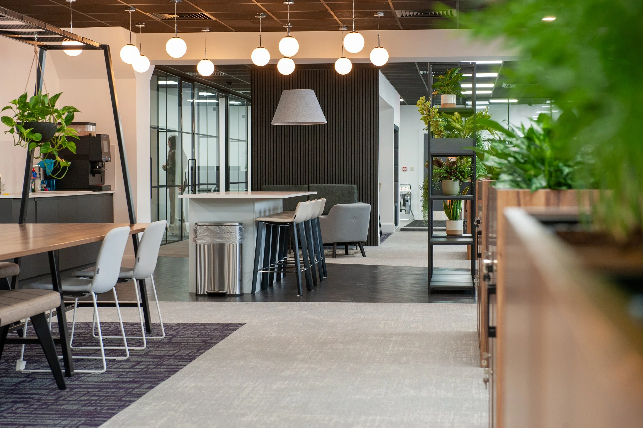 A beautifully lit interior photograph of a contemporary office refurbishment, featuring a modern open-plan workspace, sleek minimalist desks, and vibrant green indoor plants integrated into the office layout.