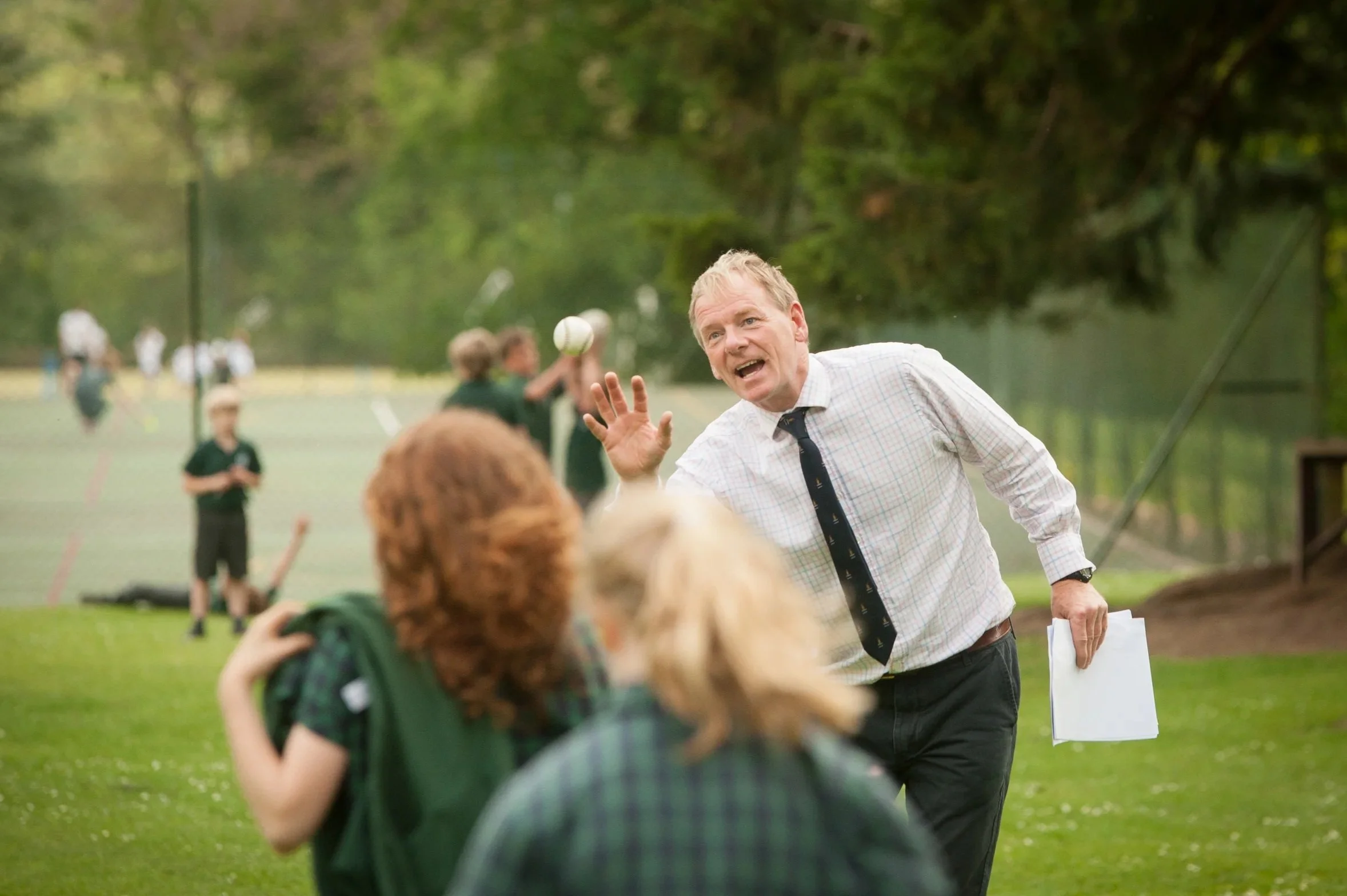 A candid prospectus photograph of a prep school headmaster instructing a young batsman on his form during a cricket match on the school grounds.