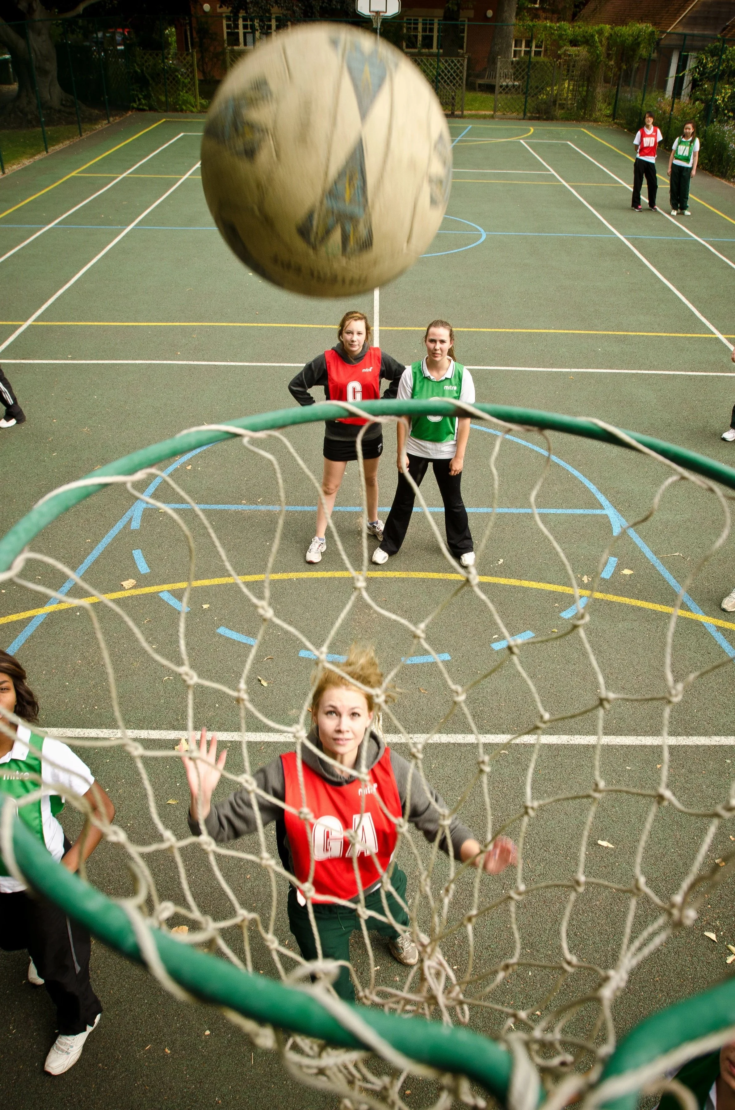 A candid action photograph of senior school students passing and defending during a netball match on an outdoor court.