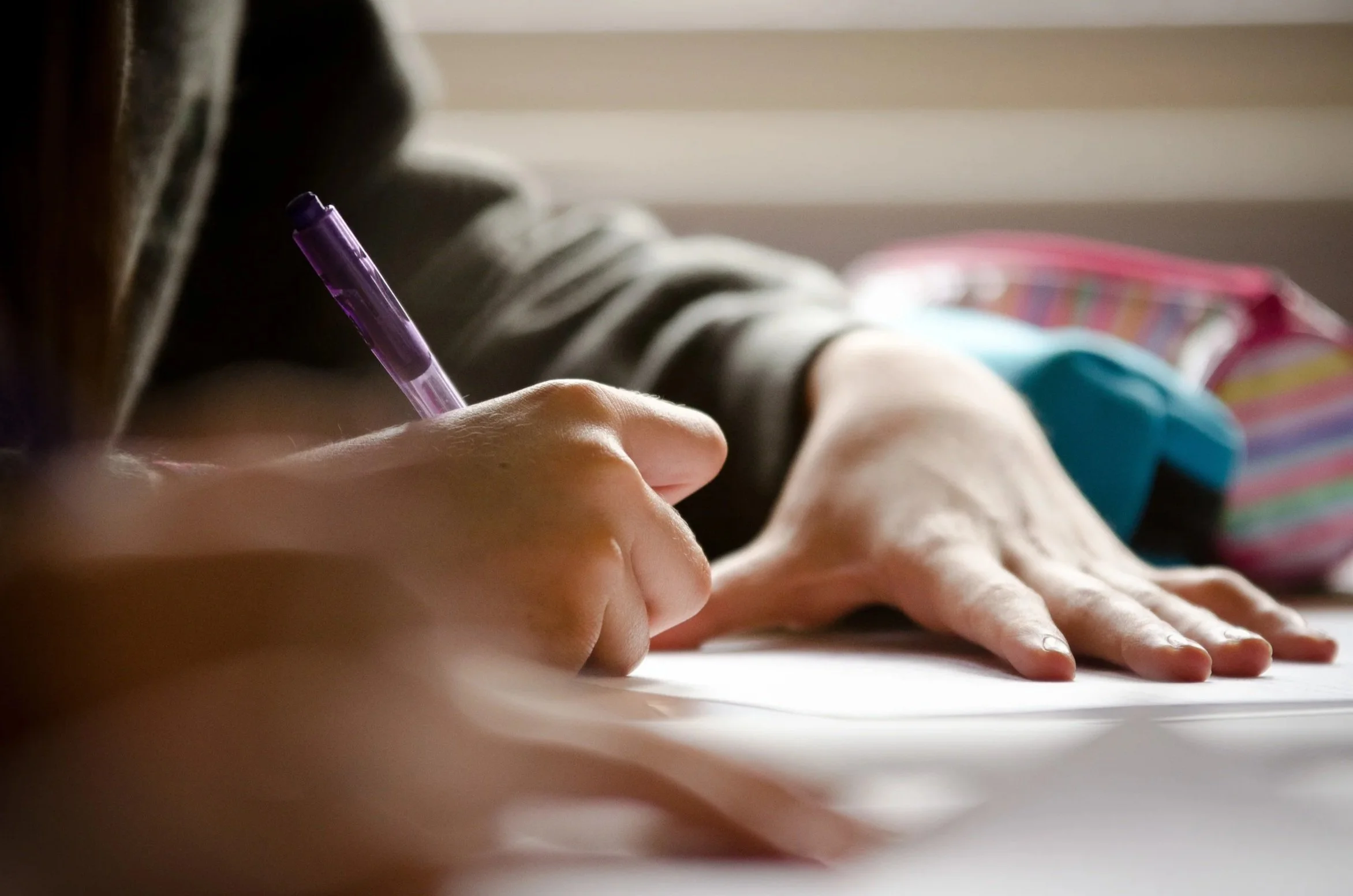Editorial education photography showing a close-up of a pupil's hand writing essay notes in a textbook, highlighting academic focus and independent study.