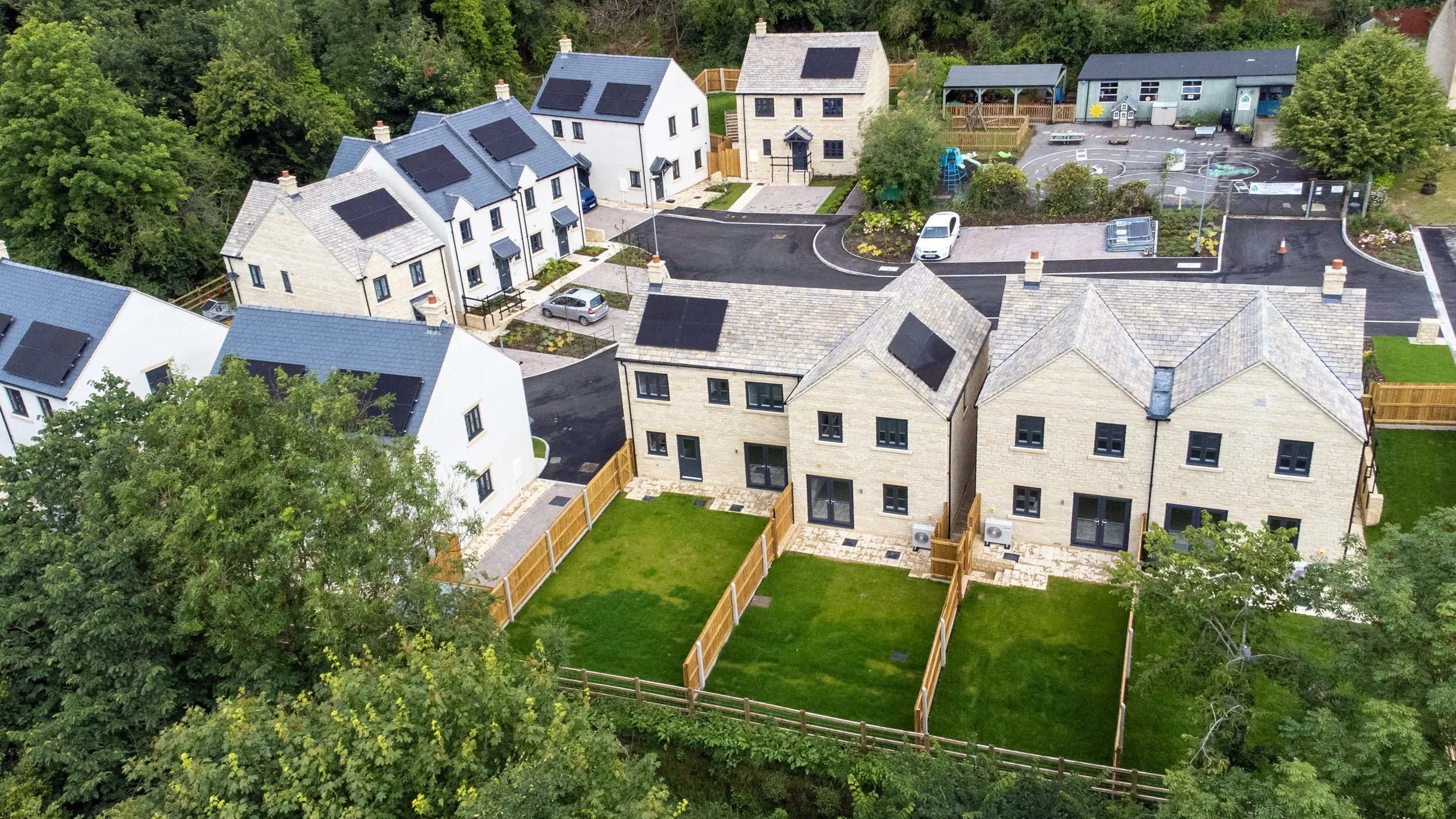 A high-angle aerial photograph of a newly developed residential area, showcasing the modern housing layout nestled within a scenic landscape with lush green surroundings