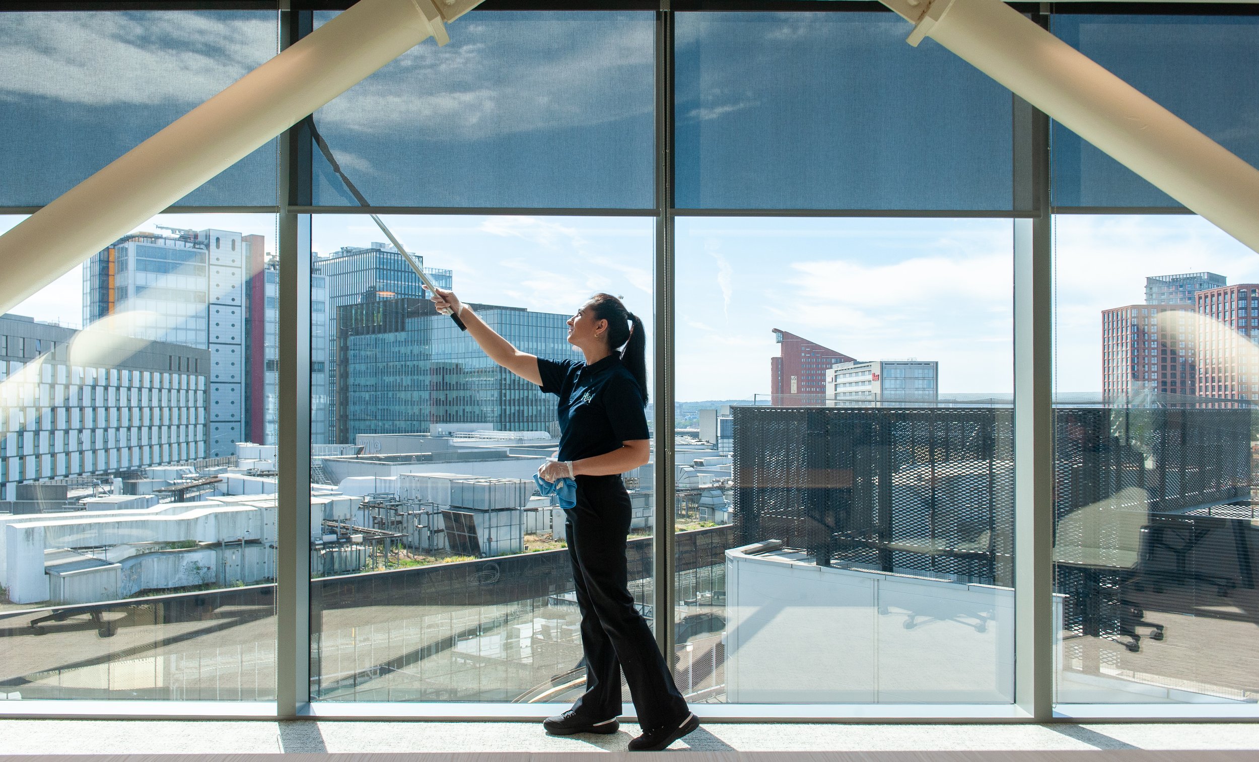 An HW Facilities team member cleaning large panoramic windows overlooking the London skyline in Stratford