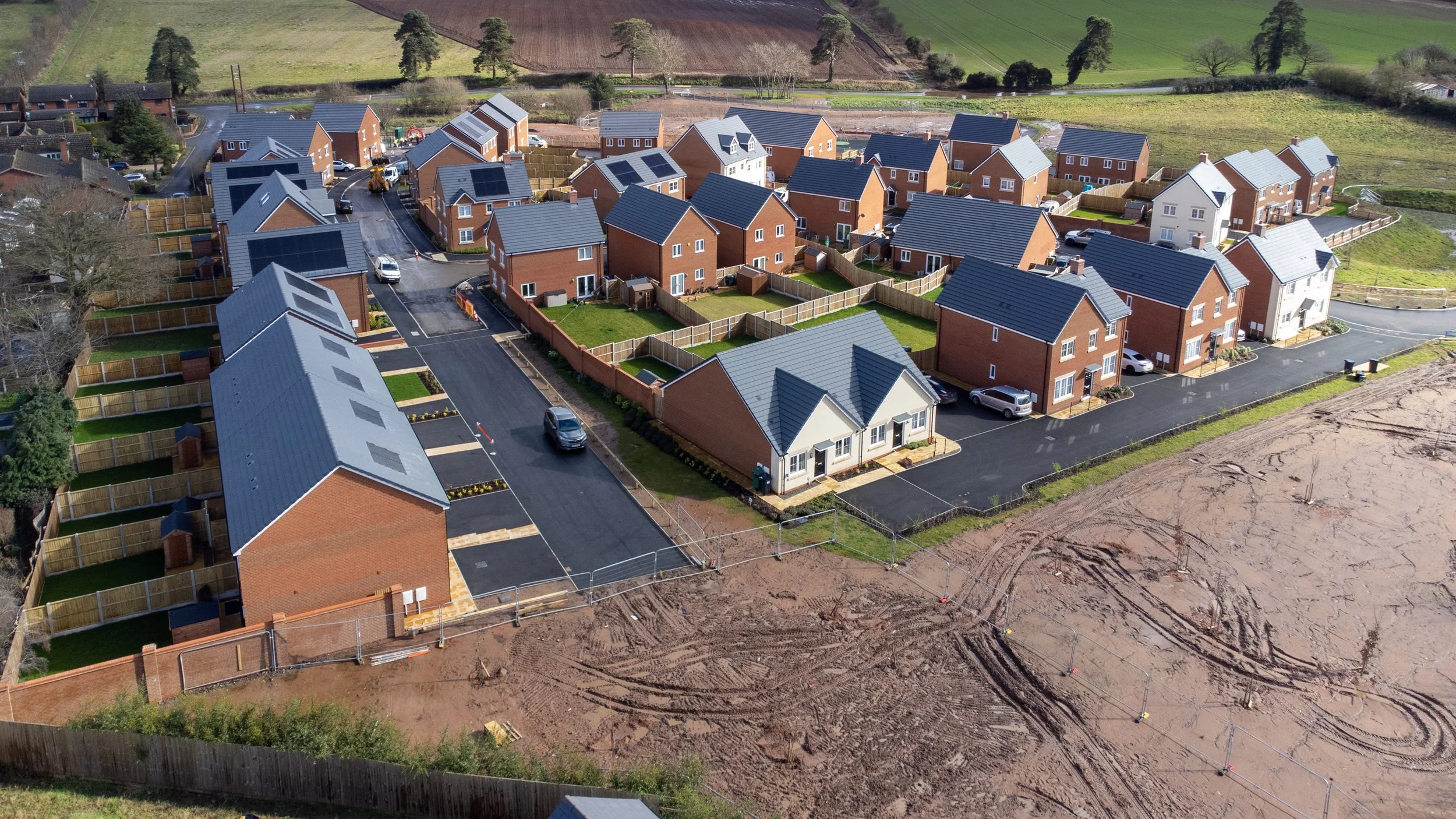 A high-angle aerial photograph of a newly developed residential area, showcasing the modern housing layout nestled within a scenic landscape.