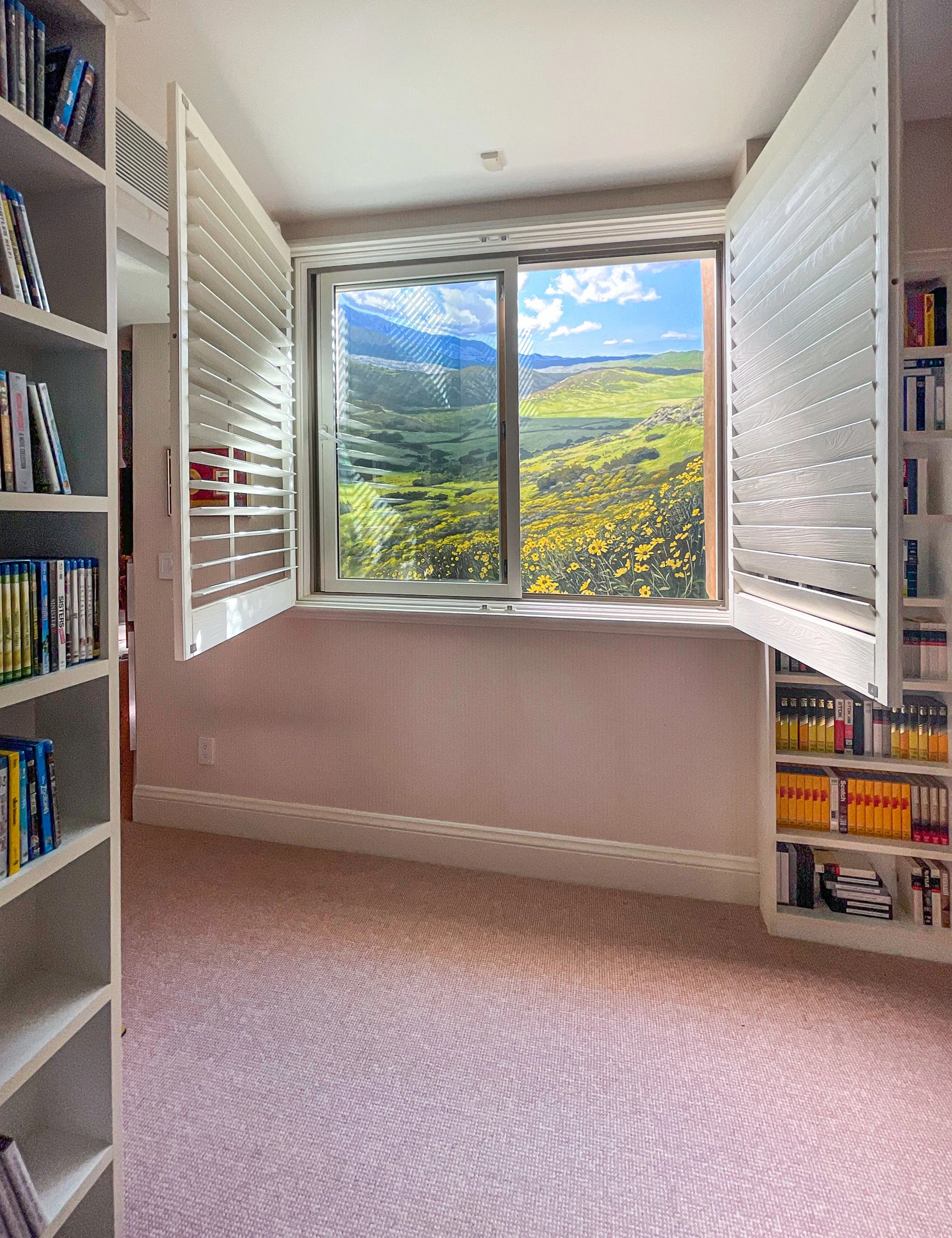 Landscape mural of rolling hills and flowers, painted on exterior egress window outside basement window.