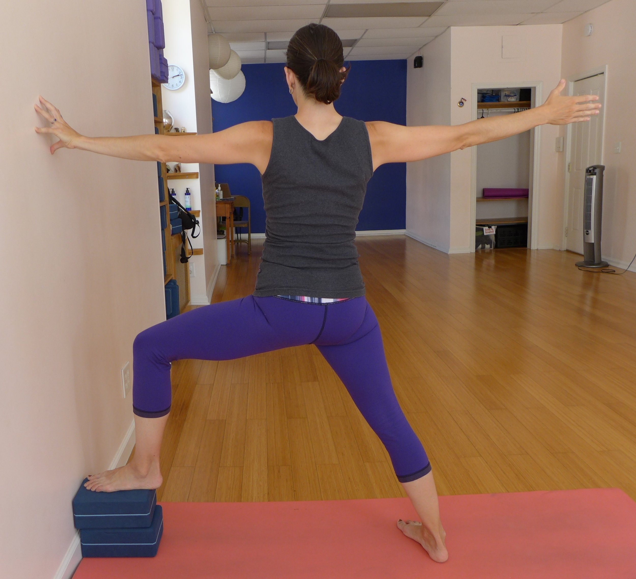 Warrior II at Wall: Warrior II can be a lot for the pelvis after childbirth. I recommend keeping this stance shorter than usual again for 6-24 weeks (or longer) after the birth. Your ligaments are still loose and you want to continue to avoid overstretching them. Here I've put two blocks under the front foot, this can help you get the opening of the inner line of the leg while keeping your stance short. Be sure to engage your outer hips here.