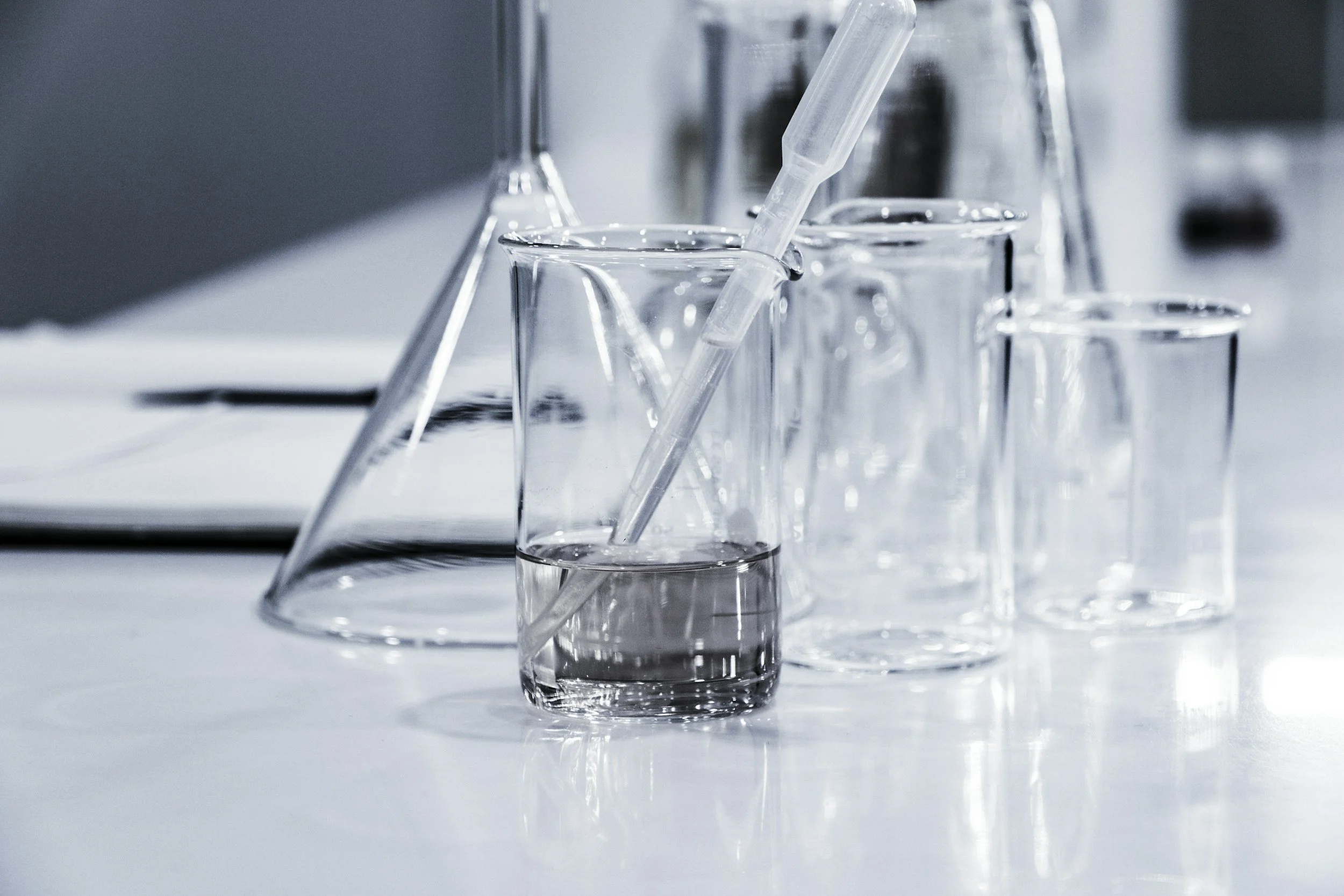 Close-up of several transparent glass test tubes and beakers, some with liquid inside, arranged on a laboratory bench.