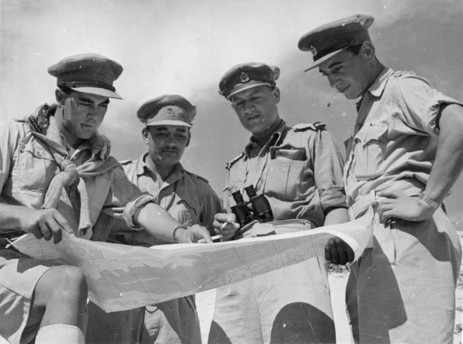 Figure 3: Behind the El Alamein front, on the eve of the successful offensive which commenced on 23 October 1942, a group of 28th Māori Battalion officers study a map of the Western Desert. Captain Hēnare is third from left. Source: National Library of New Zealand (Photographer: M D Elias), reference # DA-06727-F.