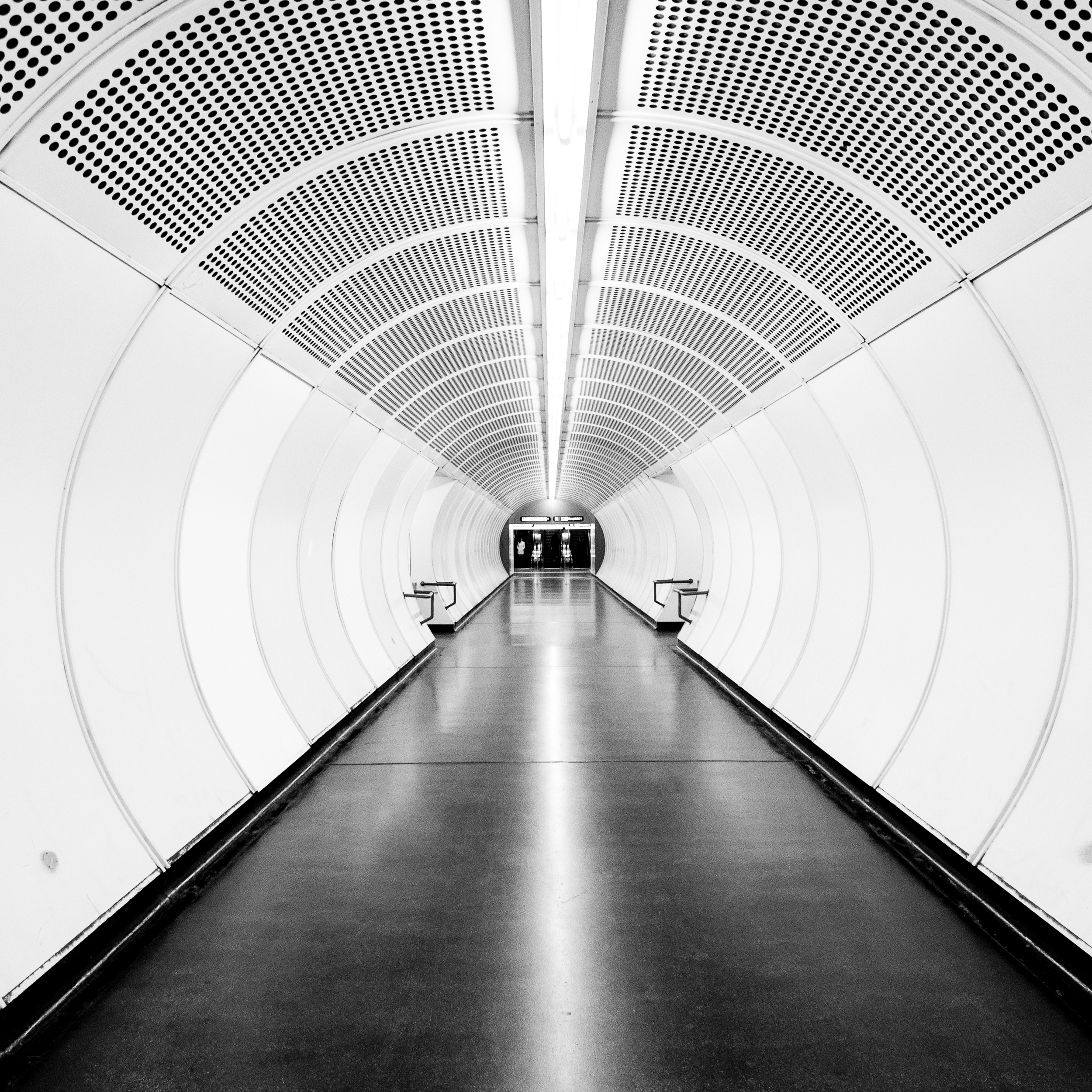 Leerer Tunnel im U-Bahnhof mit weißen Wänden und einem dunklen Boden, das Licht am Ende des Tunnels