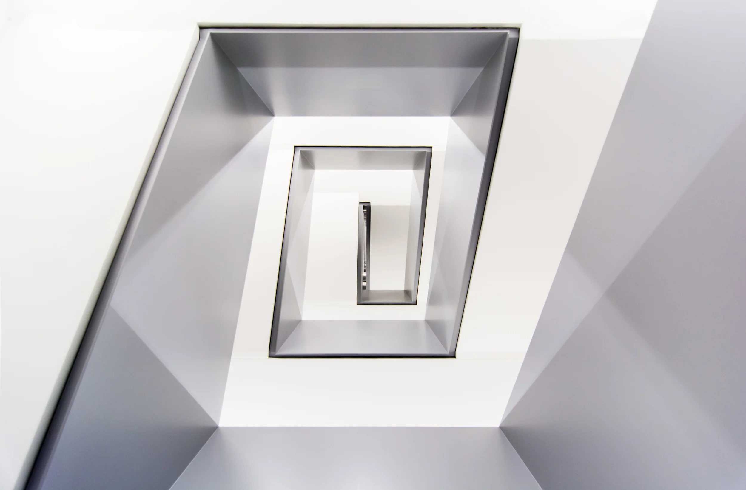 Innenaufnahme eines modernen, spiralförmigen Treppenhauses mit weißen Wänden und viereckigen Öffnungen.