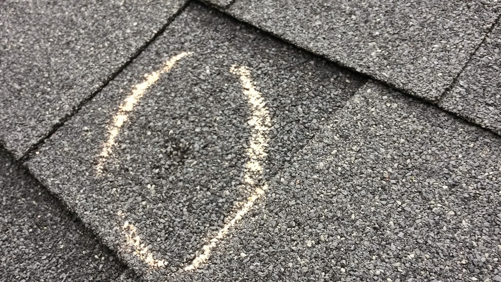 This is a hail damaged shingle. Note the indention the hail stone left and the missing granules around the mark. This impact will lead to degradation of the roofing substrate and eventually lead to leaks. 
