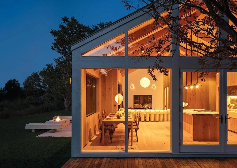 A view from outside the picture windows of a luxury kitchen and great room area with elegant lighting.