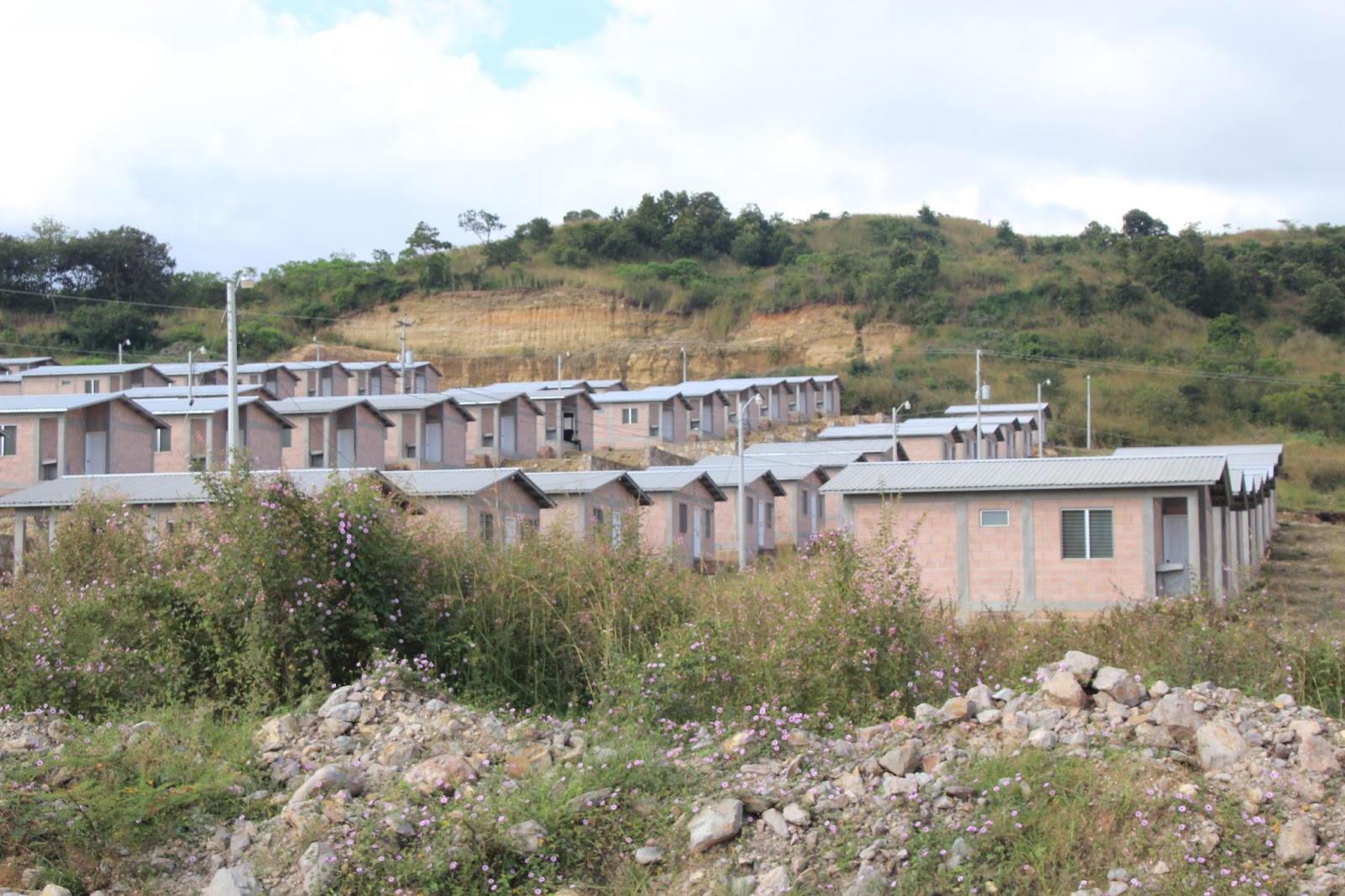 Photo caption: Approximately 120 houses built by Aura Minerals as part of an agreement with the community of Azacualpa. Aura agreed to build three different housing styles and 396 houses in total. Both the number, the styles, and additional community projects as part of the relocation process were violated by the mining company.