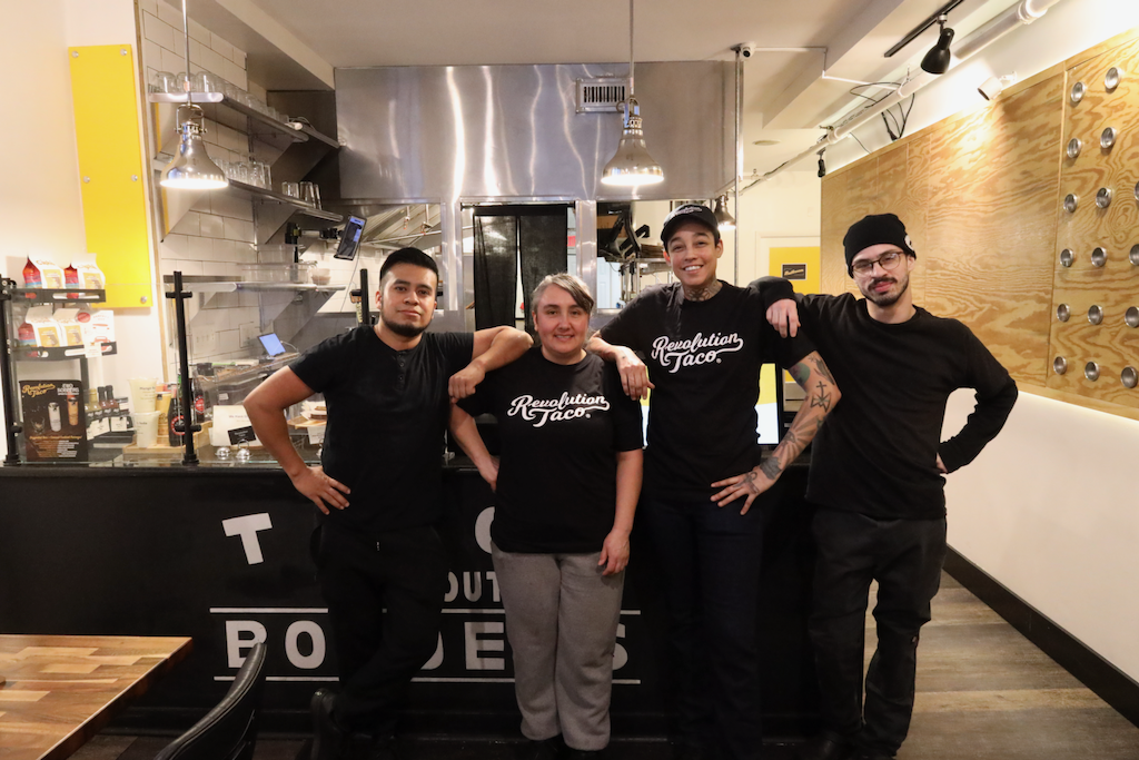 Revolution Taco team members standing together inside the restaurant kitchen, wearing black Revolution Taco shirts.