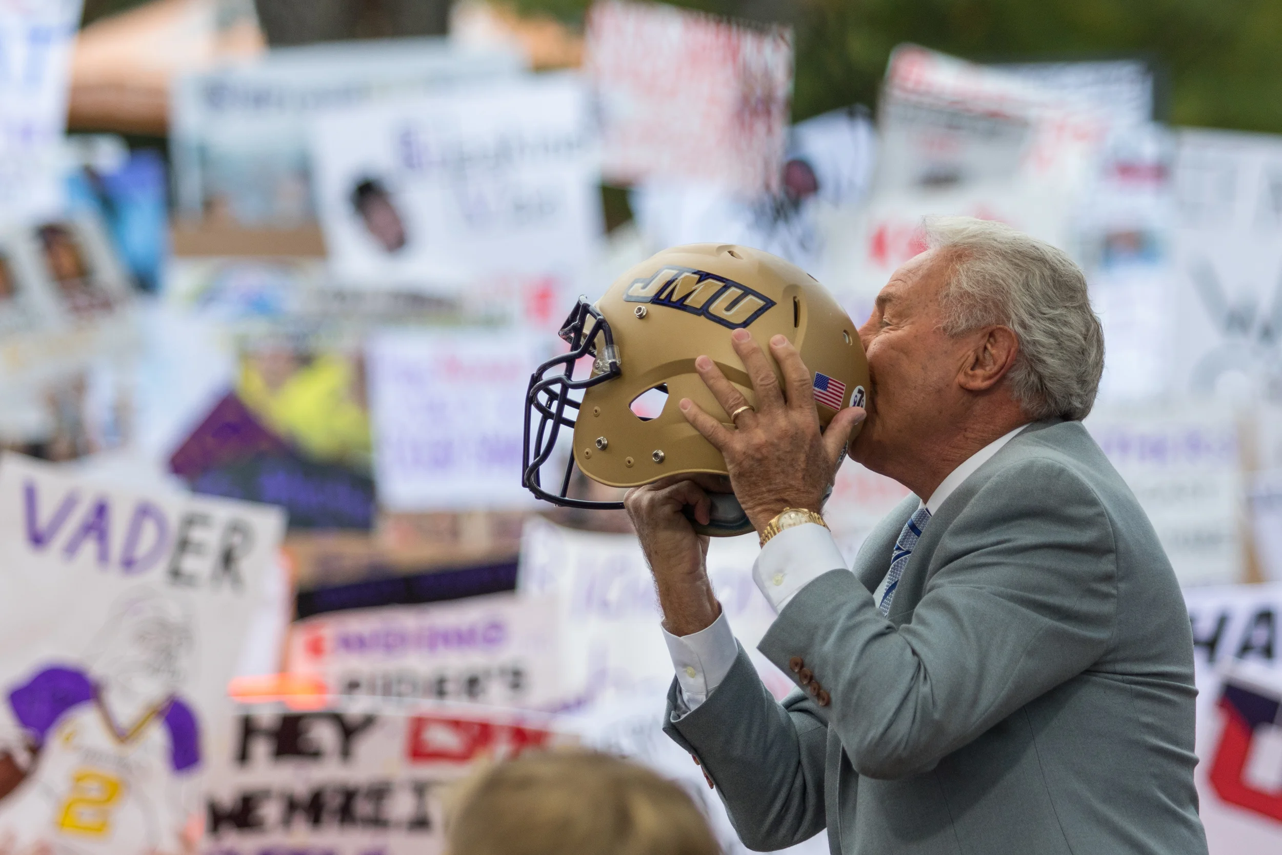 Lee Corso -ESPN Analyst and star of the show- jokes with the crowd as he holds up a JMU helmet and kisses it.