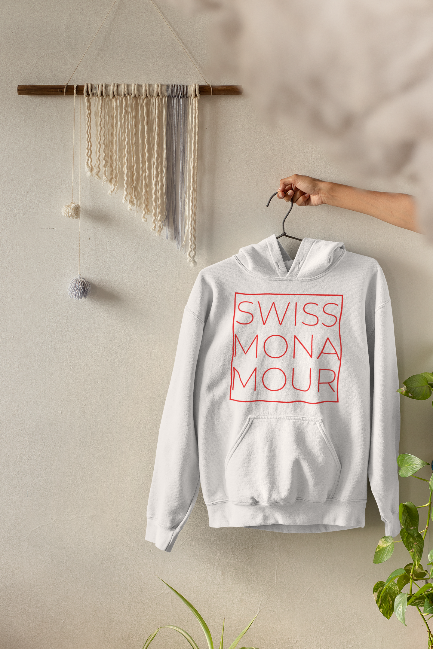 mockup-featuring-a-woman-s-hand-holding-a-pullover-hoodie-by-a-white-wall-33733.png