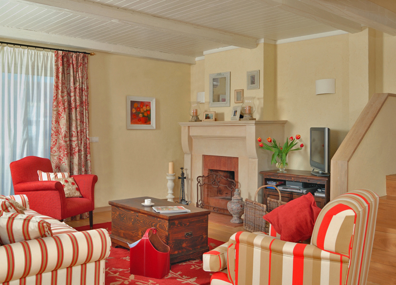 The open fire place is in lime stone, an old trunk works perfect as a coffee table. And see how the rug in red and beige is bringing all the different armchairs and the sofa together. Photo Casa Lux.