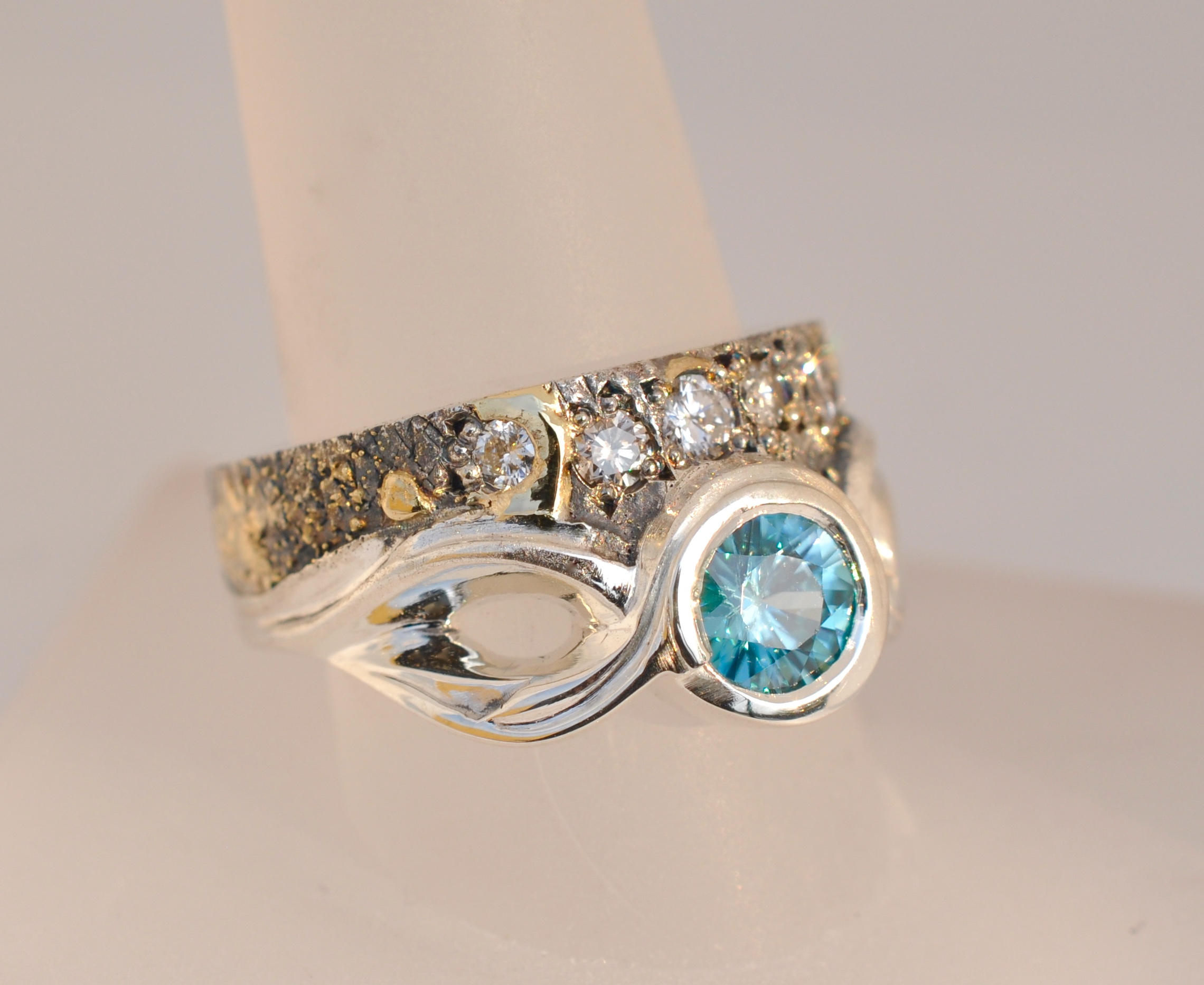 A 1.25 carat Blue Zircon is the center of attention with compliments of .45 cttw. of round brilliant diamonds, making this sculpted fusion ring a statement piece for those of a particular fashion persuasion.