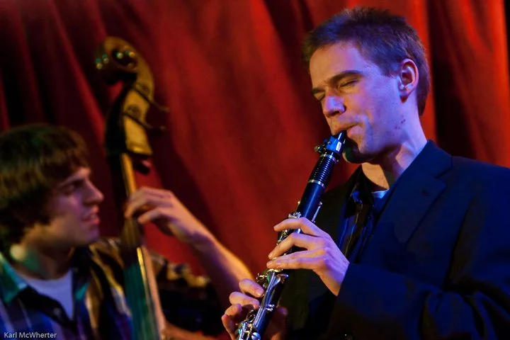 Adam Price performing clarinet on stage with a double bass player during a live jazz performance.