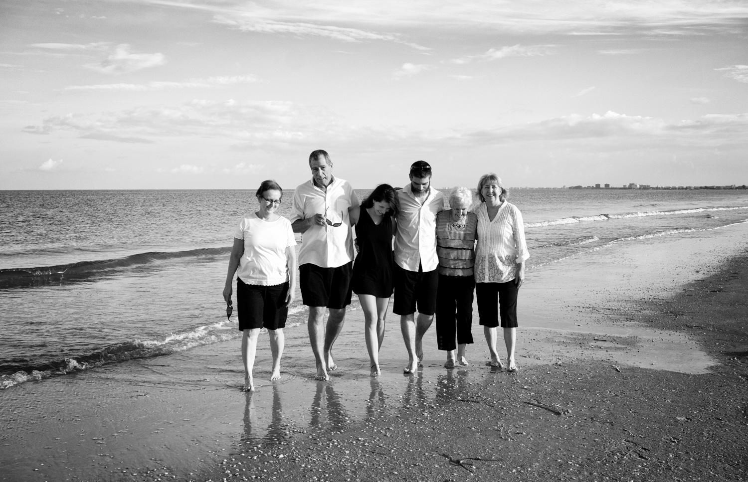 A black and white, candid family beach photo at Pass-a-Grille beach - the family walks along the shore.